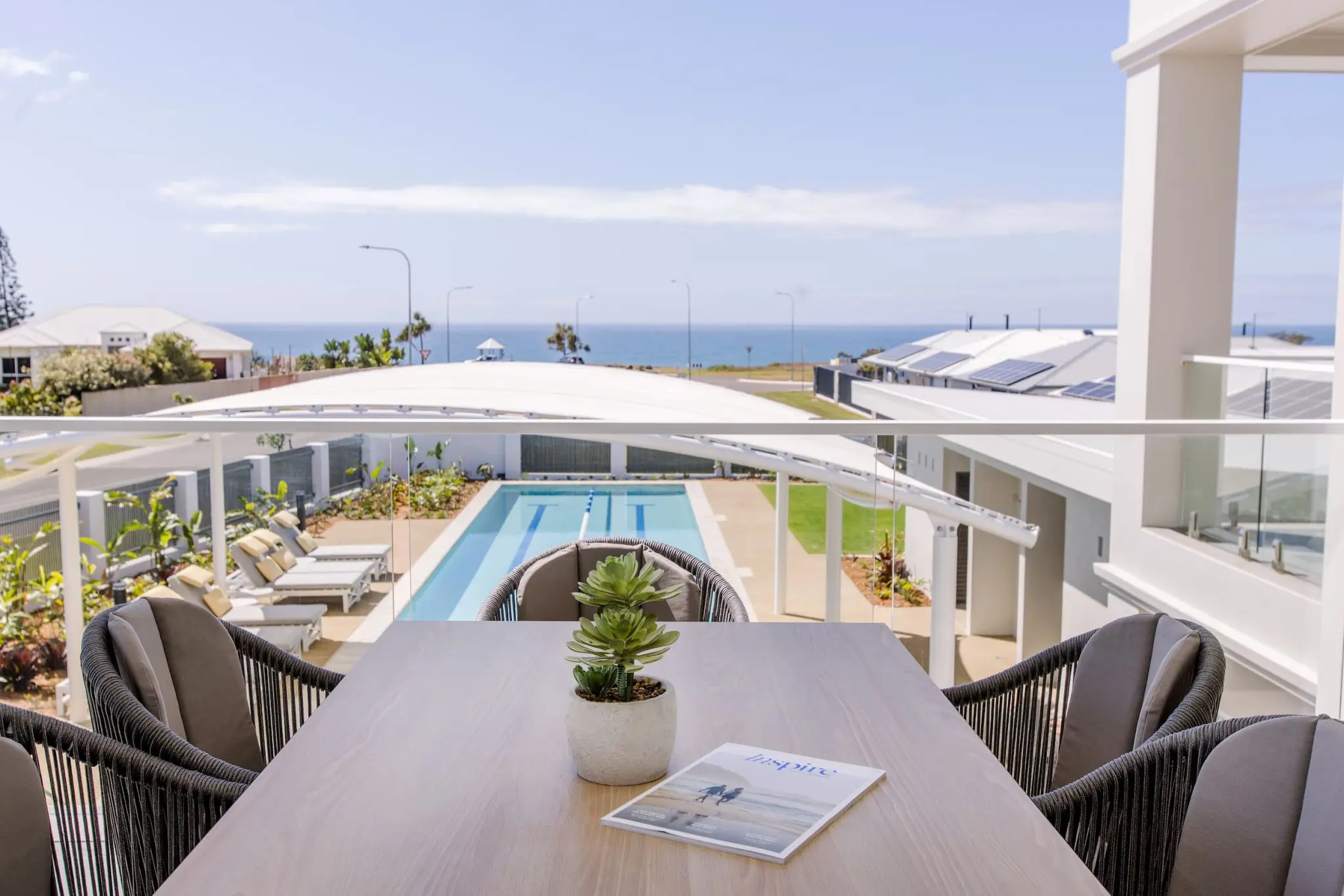 View from a balcony overlooking a pool, loungers and the ocean in an Ingenia Lifestyle community.