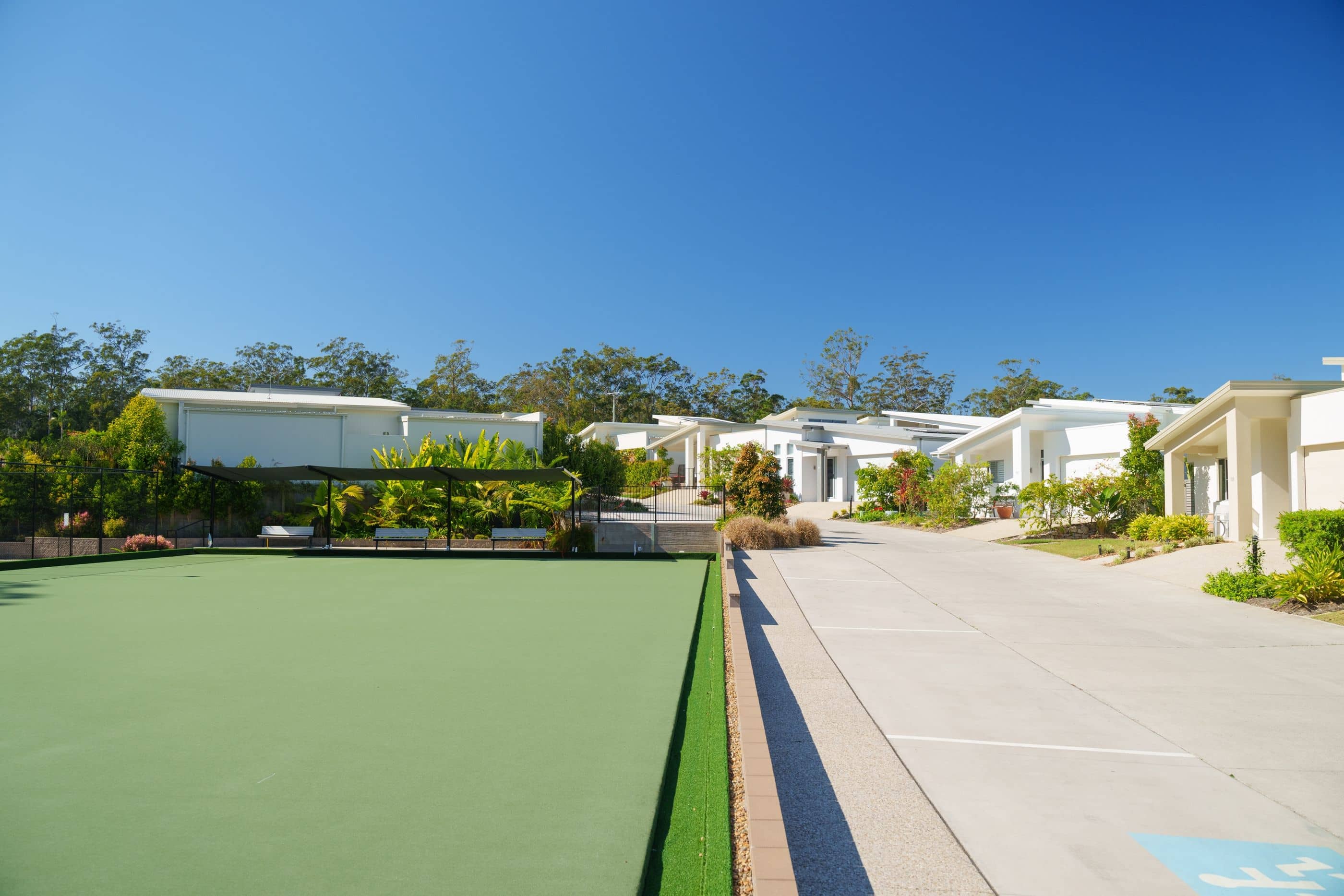 An Ingenia Lifestyle community features a green lawn bowls court with shaded seating, surrounded by modern homes and landscaped grounds.