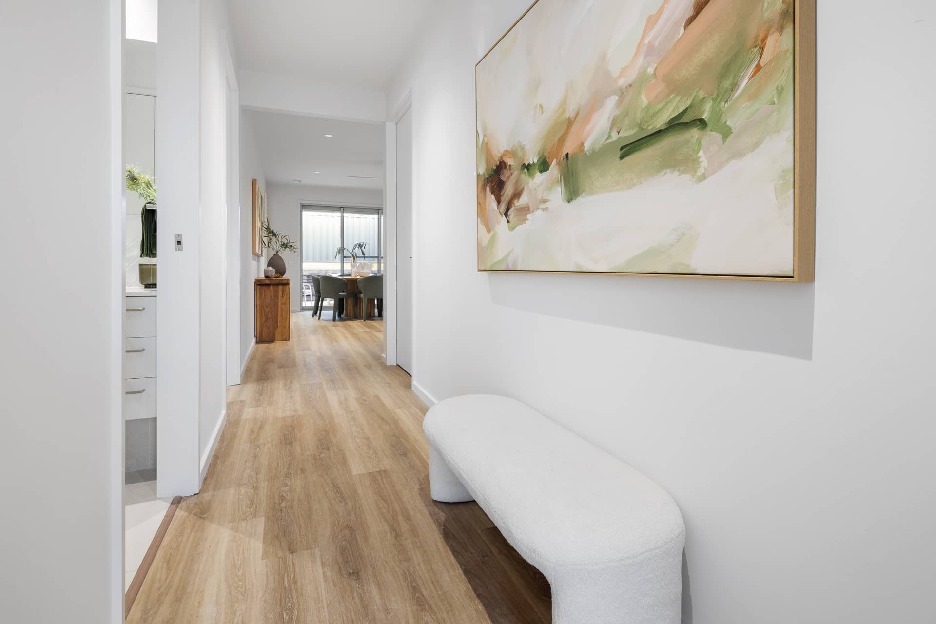Modern Ingenia Lifestyle home hallway with light wood flooring, abstract art, and a white textured bench.