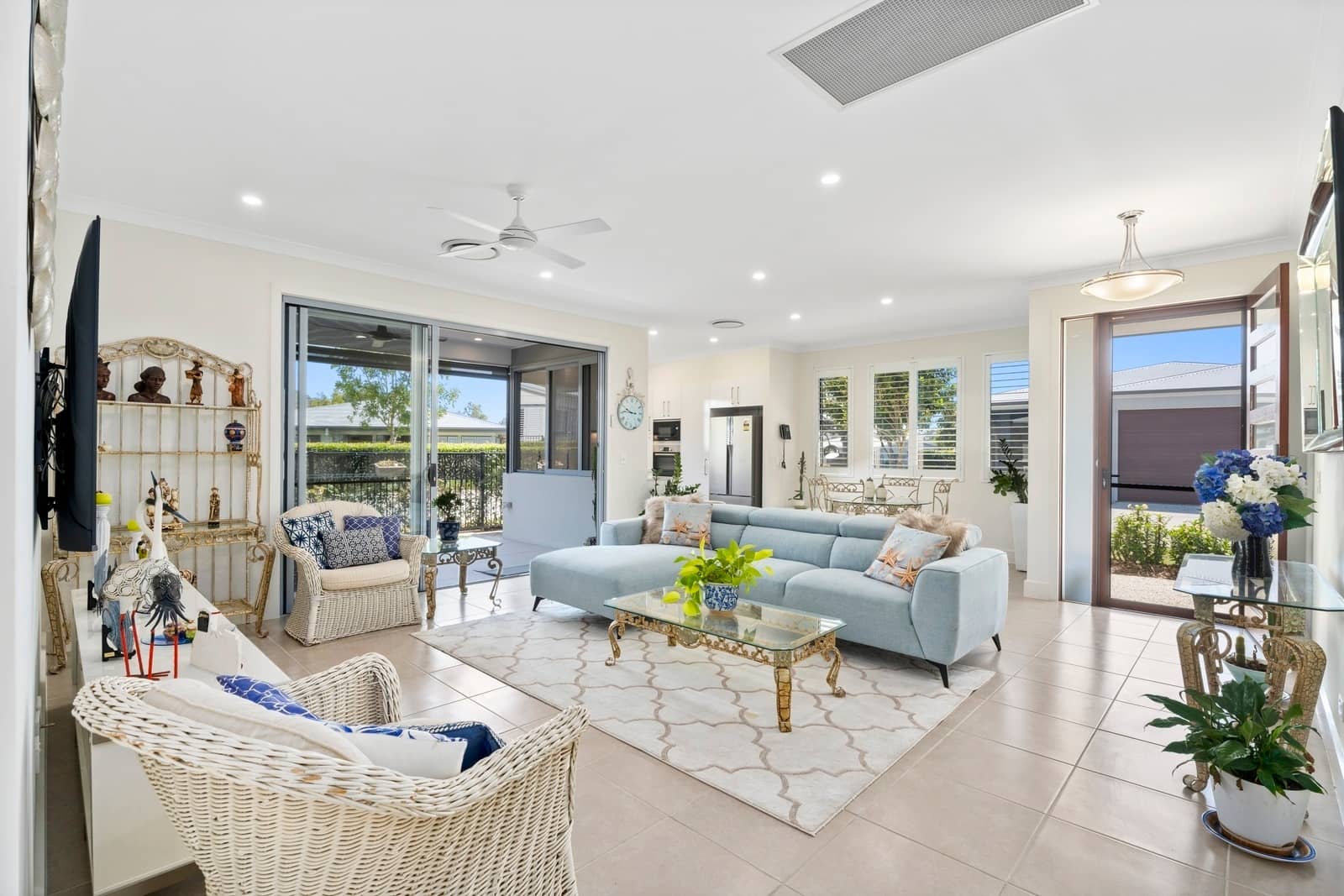 Bright open-plan living room of an Ingenia Lifestyle home with light blue sofa, wicker chairs, and patio doors.