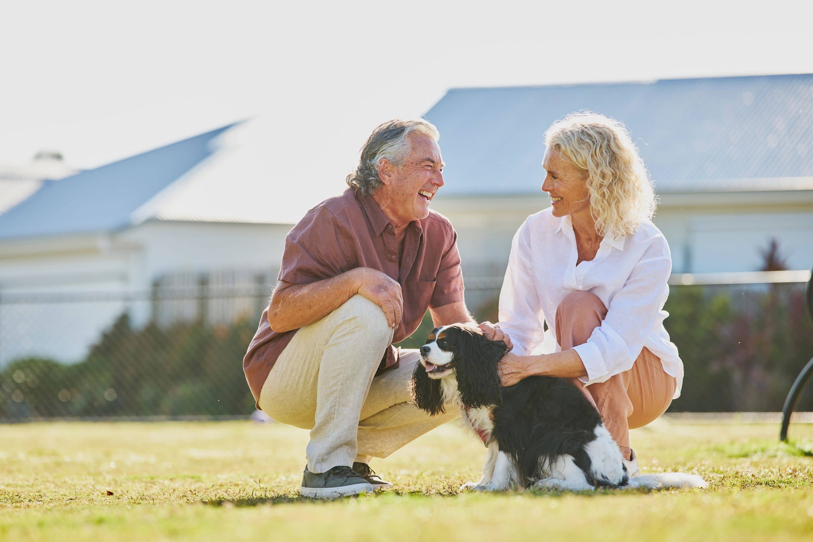 A couple crouches on a lawn, petting a black and white dog.
