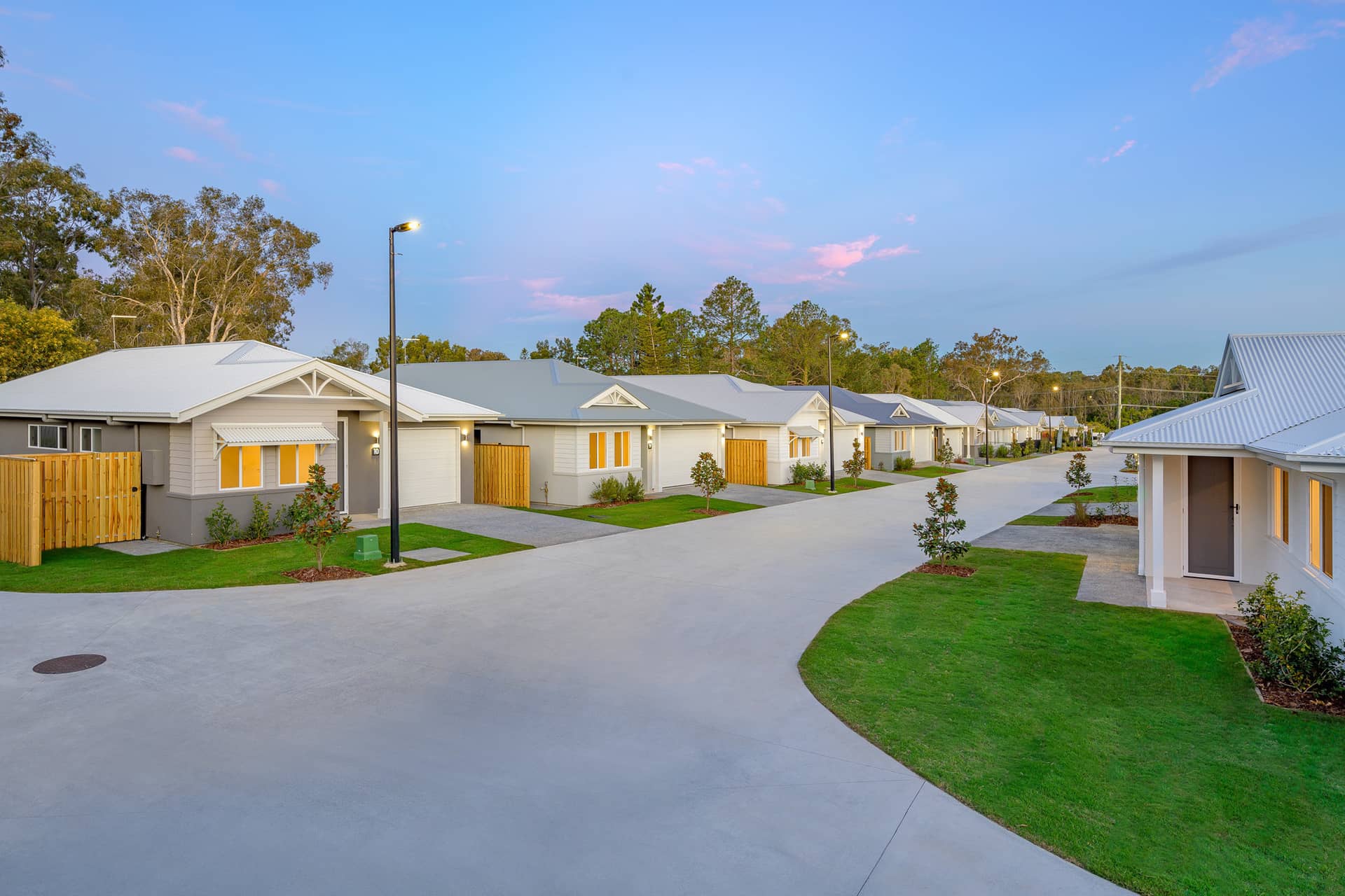 Street view of modern, low-maintenance homes in an Ingenia Lifestyle community with landscaped grounds and streetlights at dusk.
