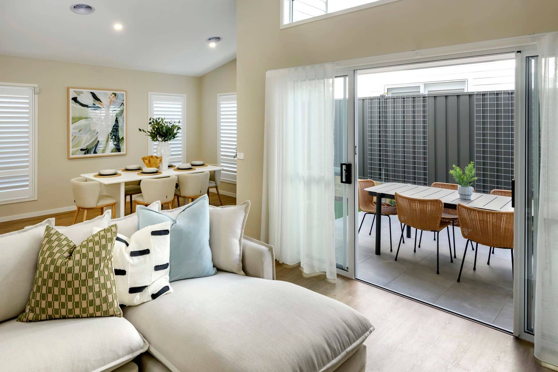 A modern lounge area with a chaise and dining room visible through sliding glass doors to an outdoor seating area.