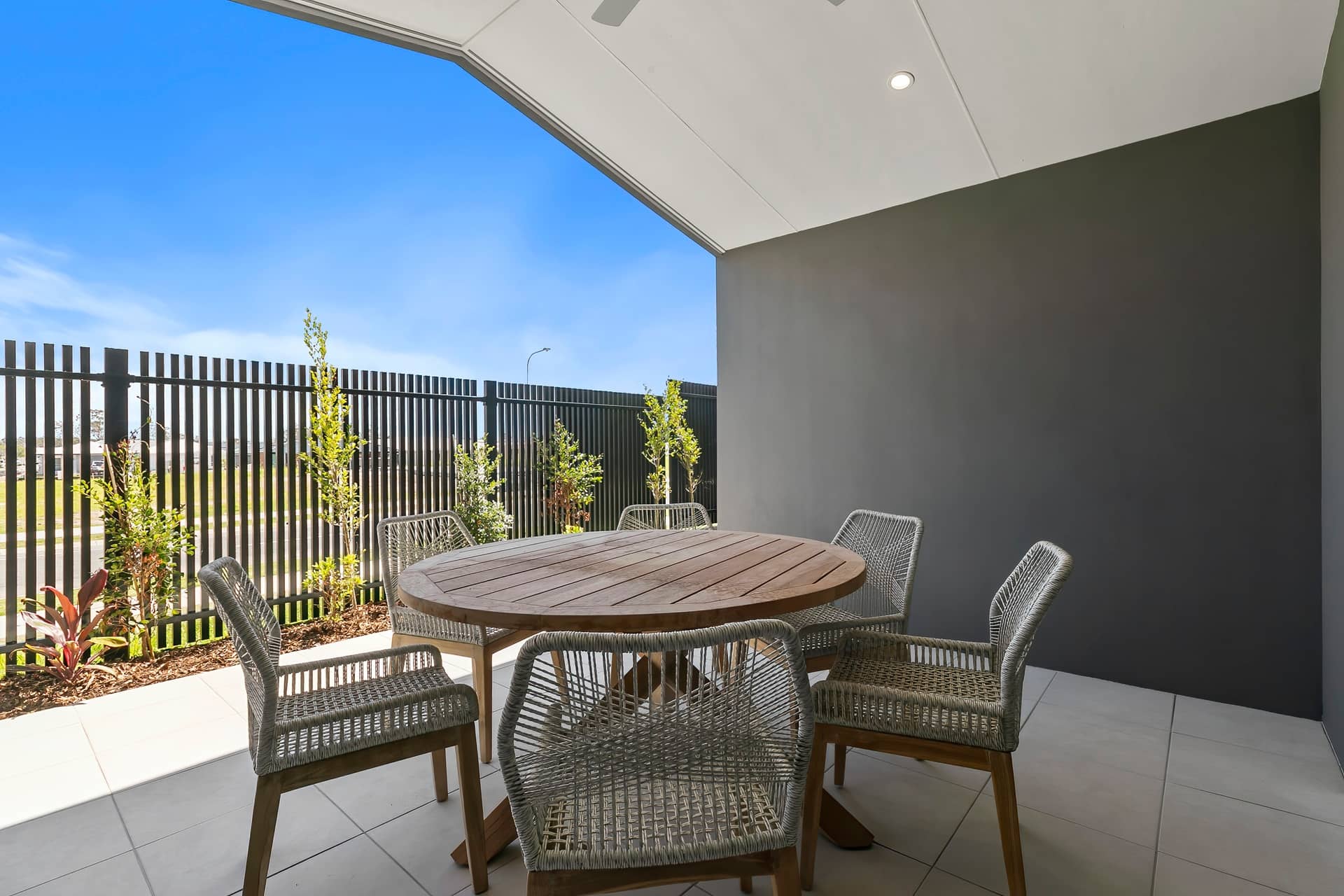 Outdoor patio of an Ingenia Lifestyle home featuring a wooden table, woven chairs, tiled floor, and landscaped garden.