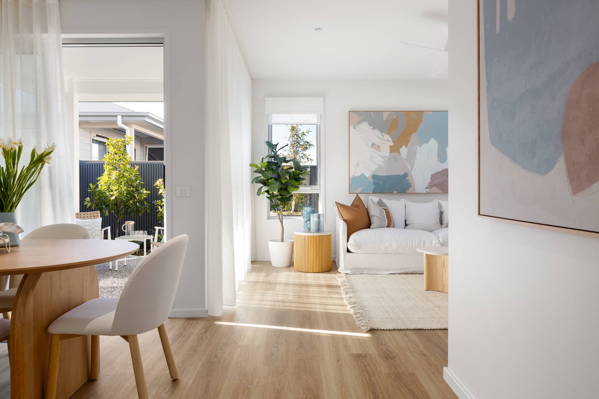Open-plan living and dining area in an Ingenia Lifestyle home, with a sofa, wood table, and bright outdoor access.