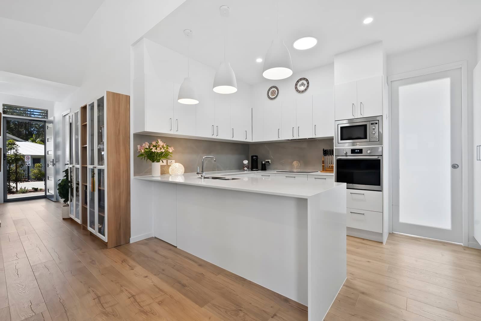 Modern white kitchen in an Ingenia Lifestyle home, featuring a large island, stainless steel appliances, and light timber flooring.