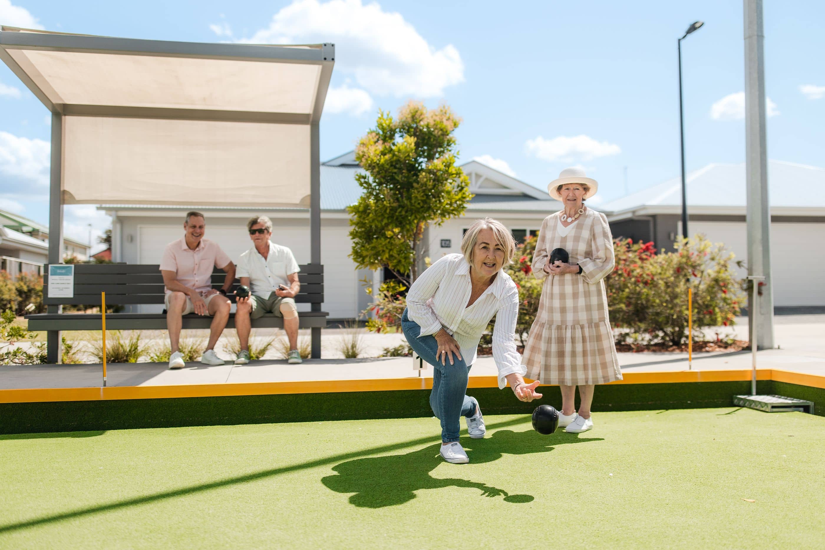 Four Ingenia Lifestyle residents playing lawn bowls at a community facility. A woman rolls a bowl while others watch.