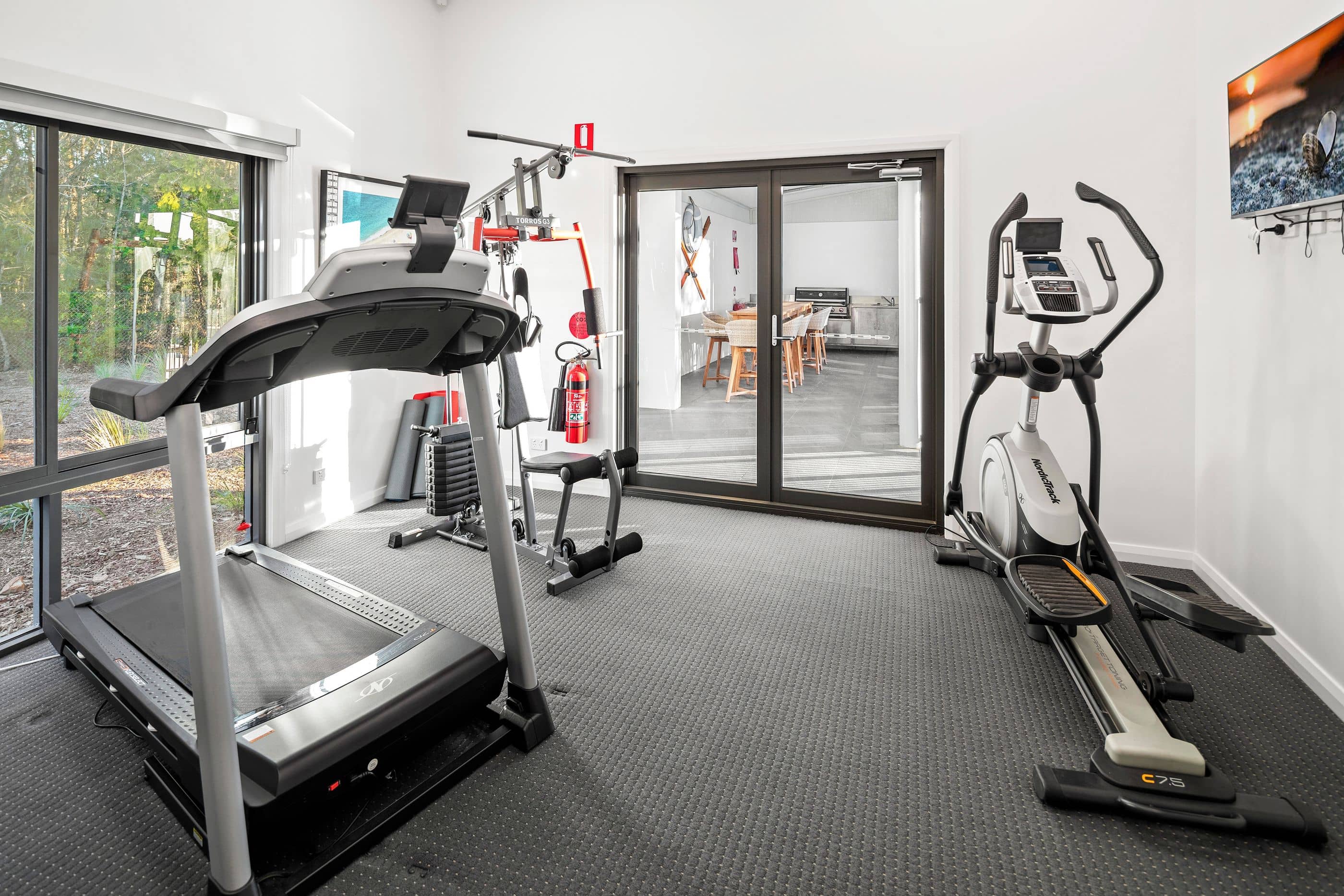 Interior view of a home gym in an Ingenia Lifestyle community, featuring a treadmill, elliptical, and weight machine.
