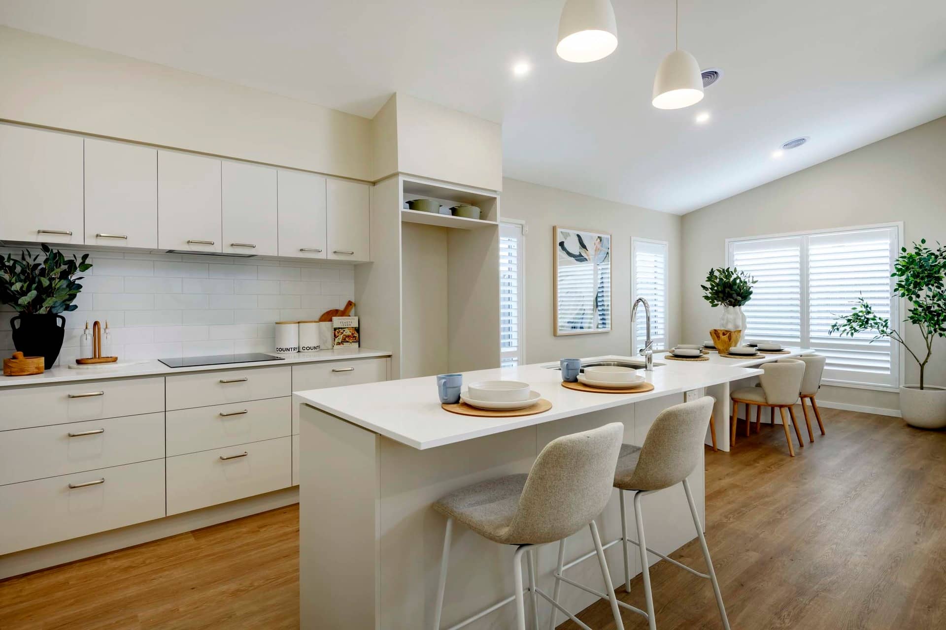 A modern kitchen with white cabinetry, a white island with bar stools, and a dining area.
