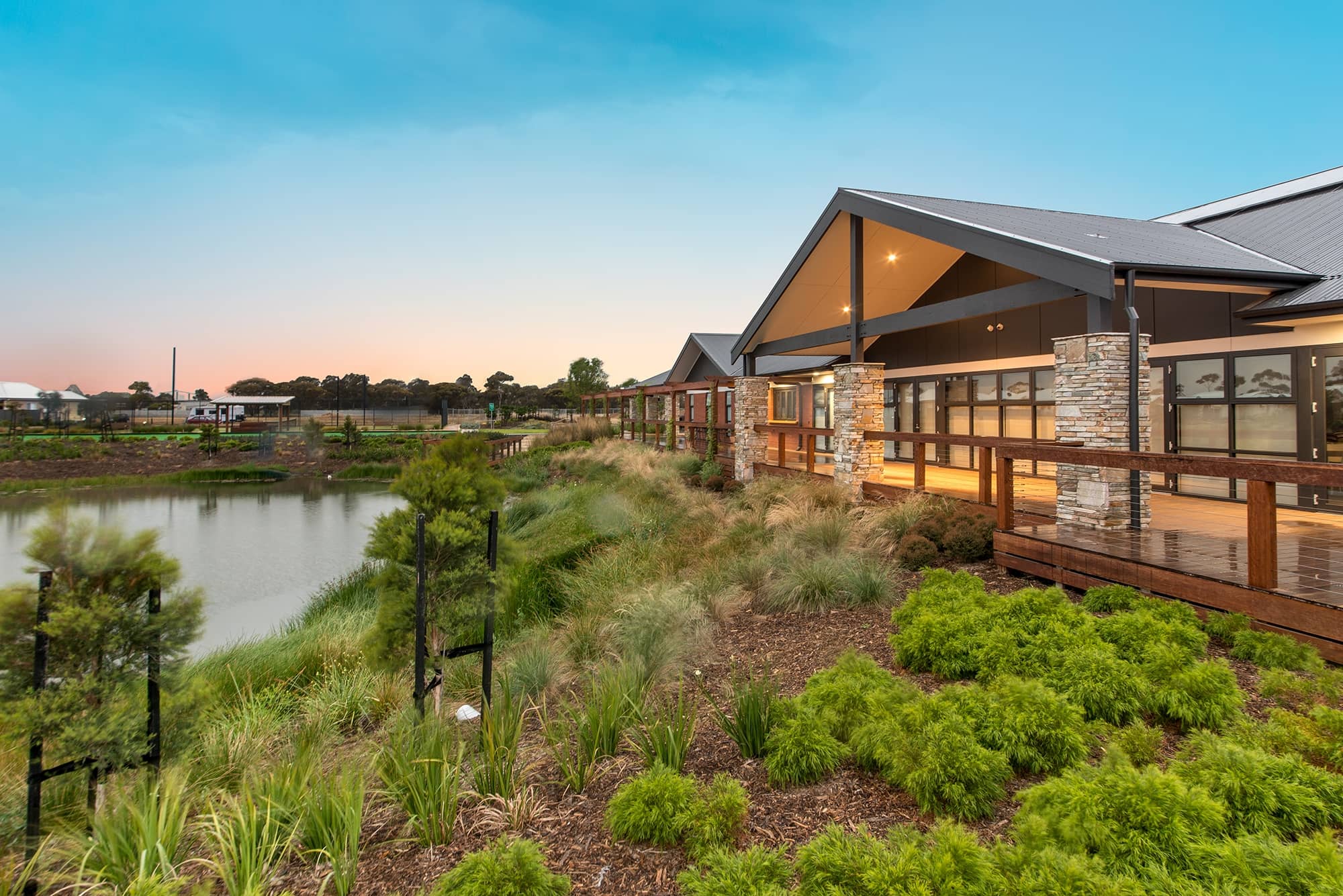 Modern community building with a wooden deck overlooking a lake, at dusk.