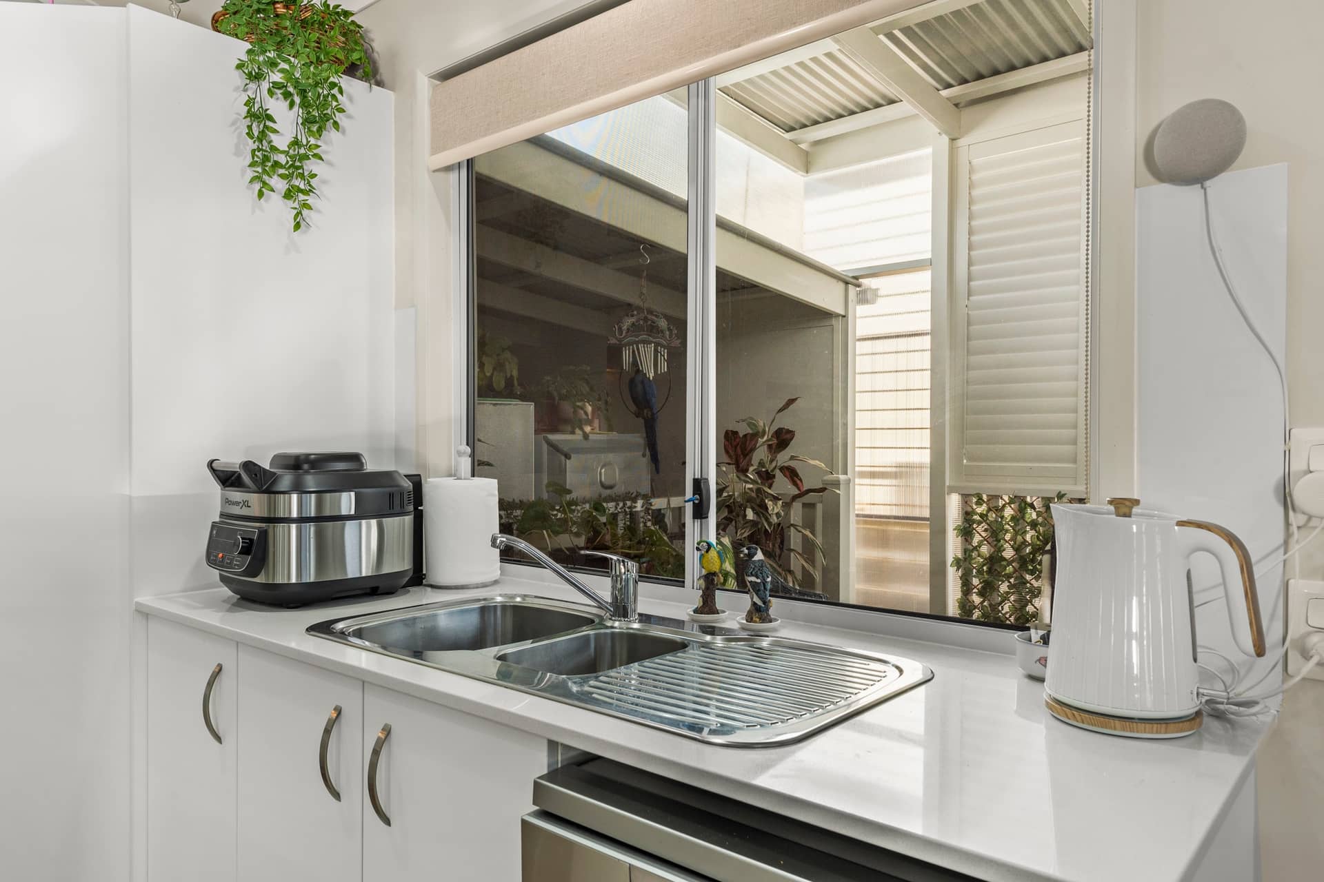 Modern kitchen in an Ingenia Lifestyle home with white cabinetry, a double sink, and view to a private outdoor area.