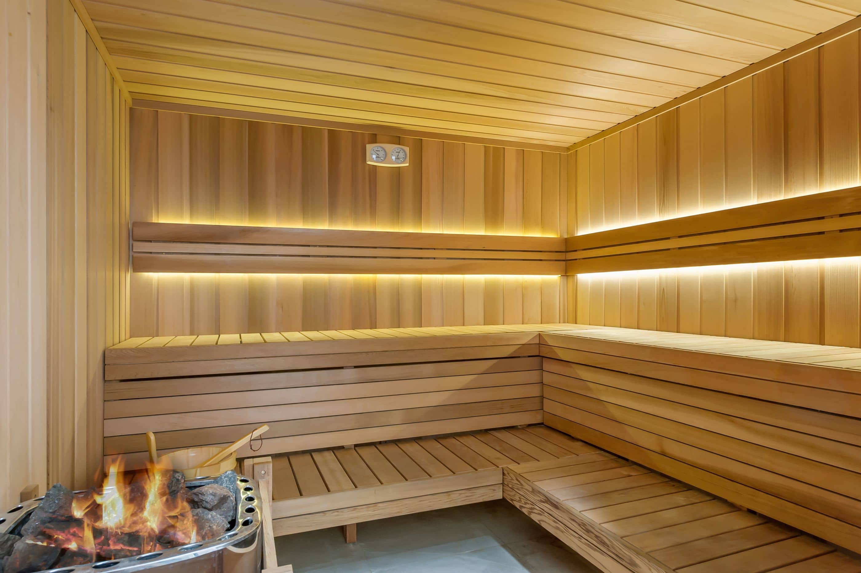 Interior of a timber sauna with tiered benches, subtle lighting, and a sauna heater with glowing stones, a community shared amenity.