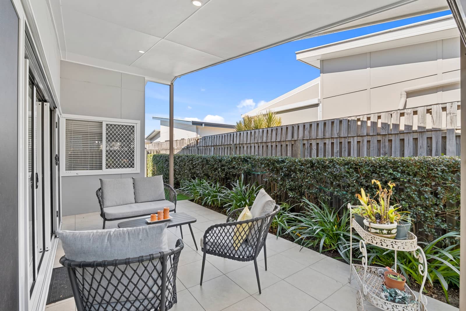 A covered patio with outdoor furniture faces a low-maintenance garden and fence.