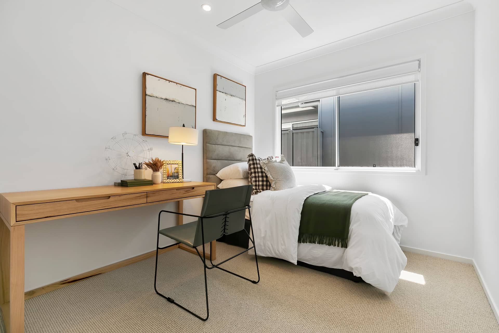 A bright bedroom in an Ingenia Lifestyle home with a wooden desk, bed with white bedding, and light carpet.