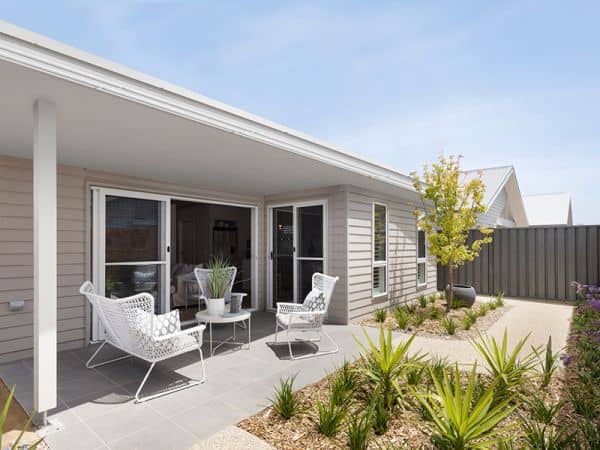 Covered outdoor patio of an Ingenia Lifestyle home with white seating, sliding doors, and a low-maintenance landscaped garden.