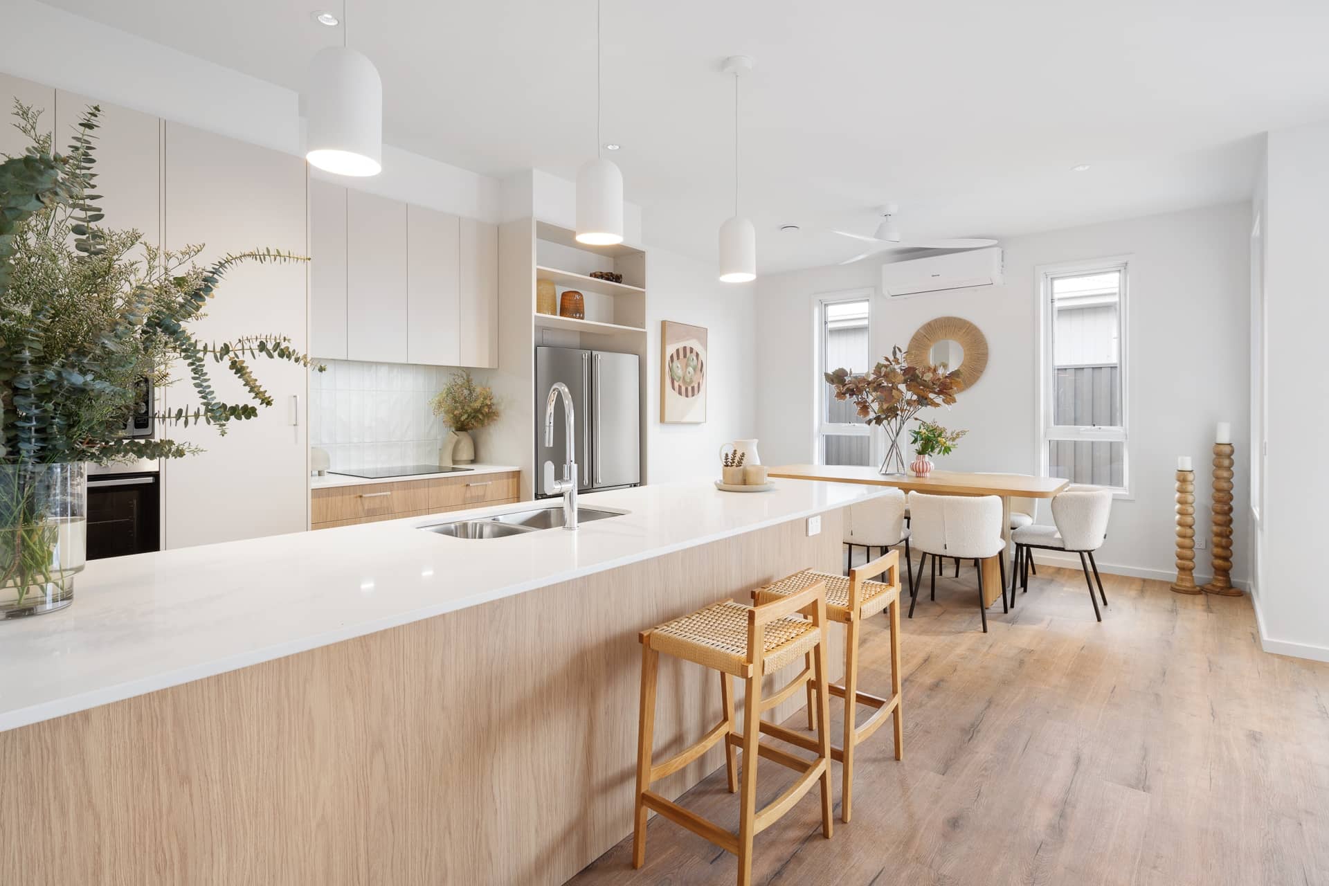 Bright, open-plan kitchen and dining area in an Ingenia Lifestyle home. Features a large island bench with a sink, light timber cabinetry, modern appliances, and a dining table with chairs.