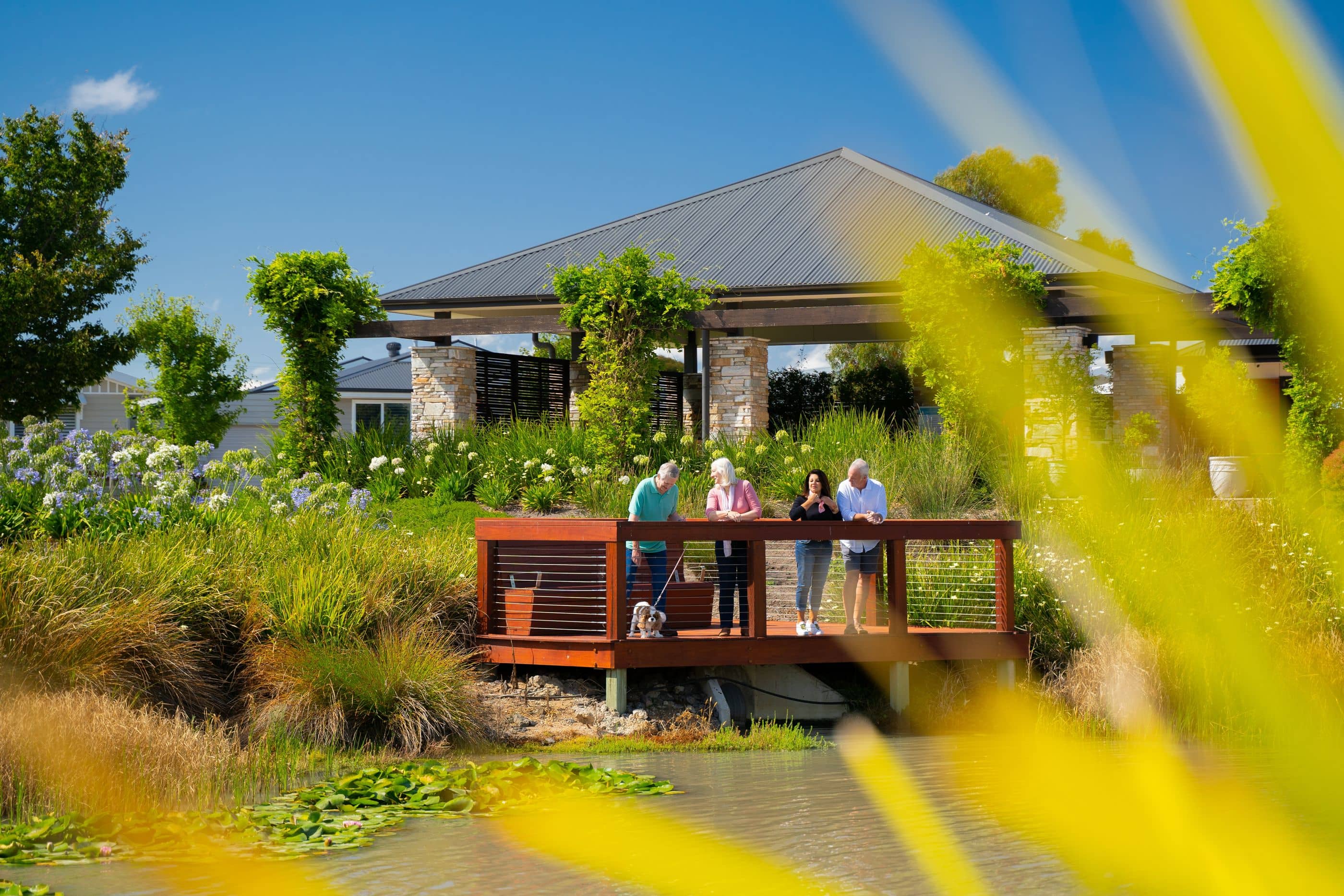 People gathered on a deck overlooking a pond with lily pads and surrounding gardens in an Ingenia Lifestyle community.