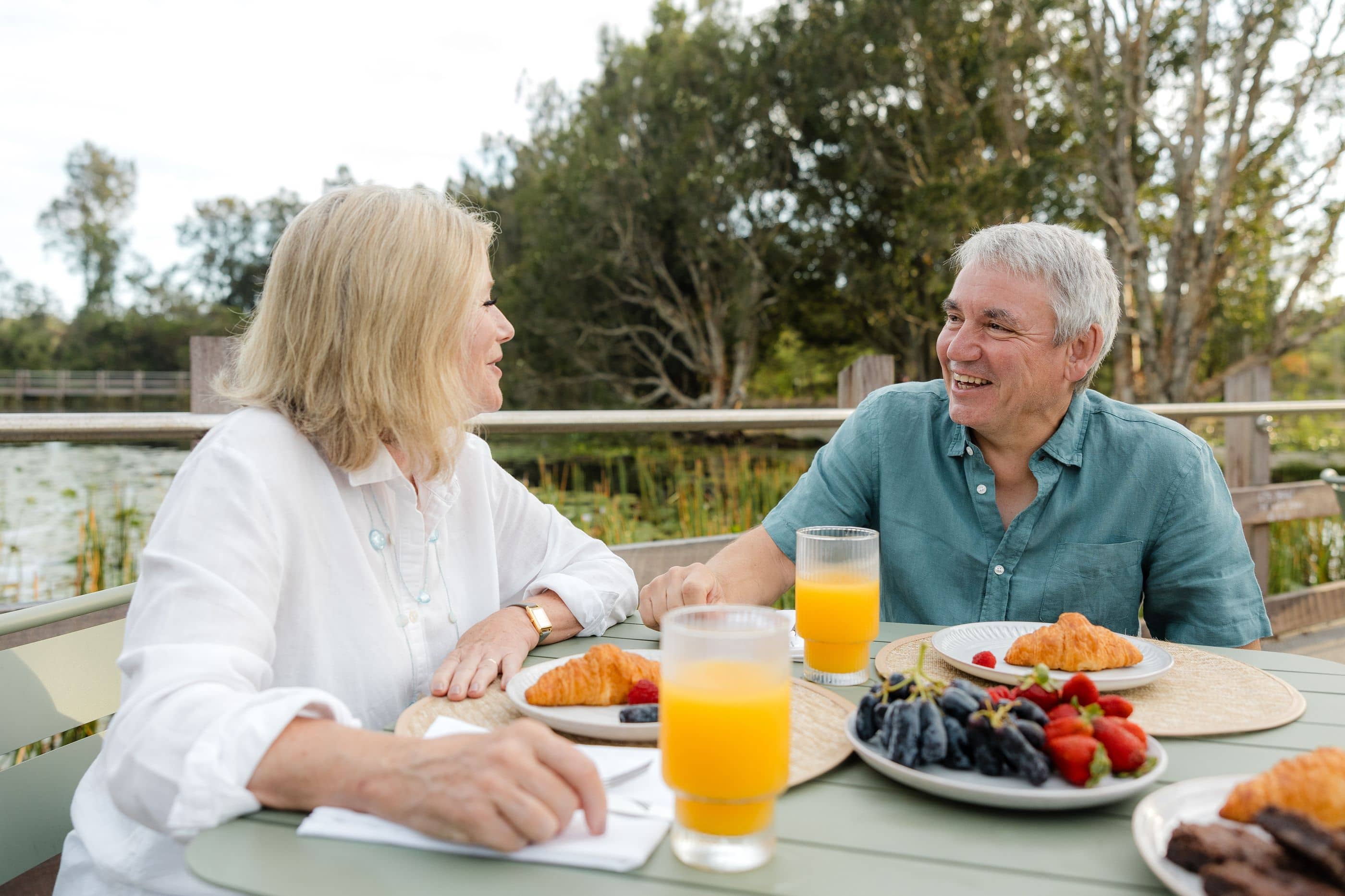 Two people look at each other enjoying breakfast outside.