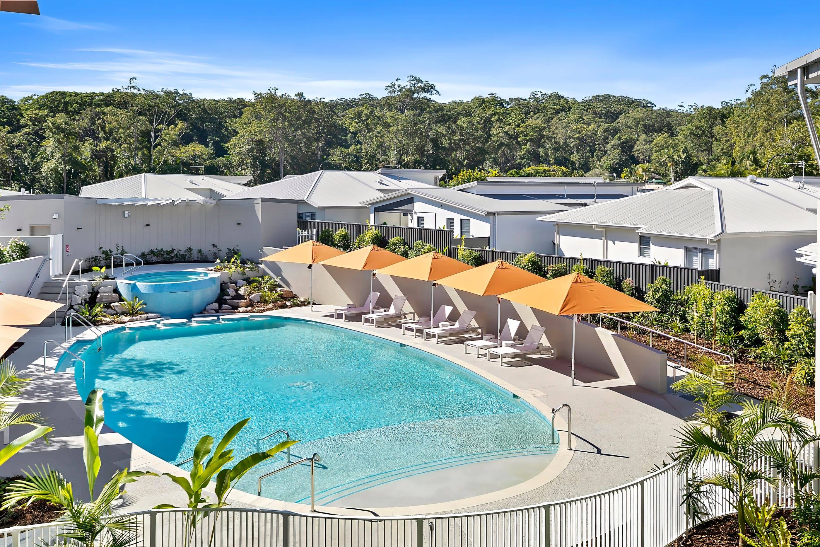 Ingenia Lifestyle community pool and spa, featuring sun lounges, umbrellas, modern homes, and lush green landscaping.