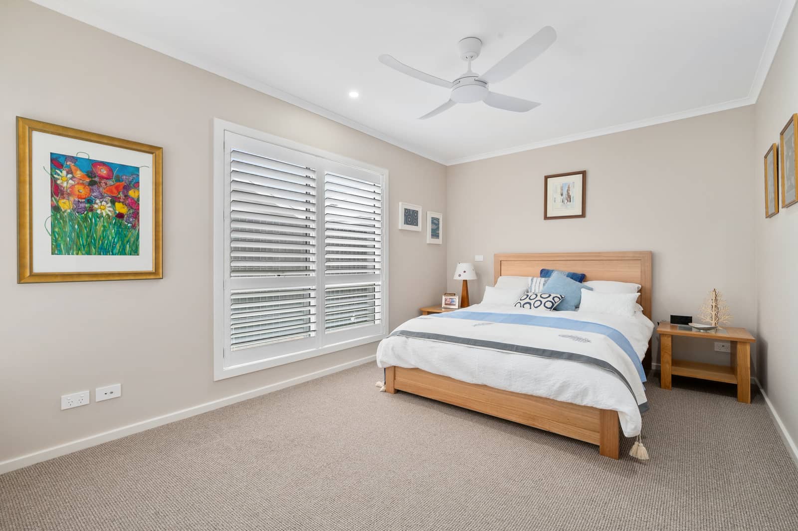 Bedroom in an Ingenia Lifestyle home with a wooden bed, neutral carpet, ceiling fan, and window with white shutters.