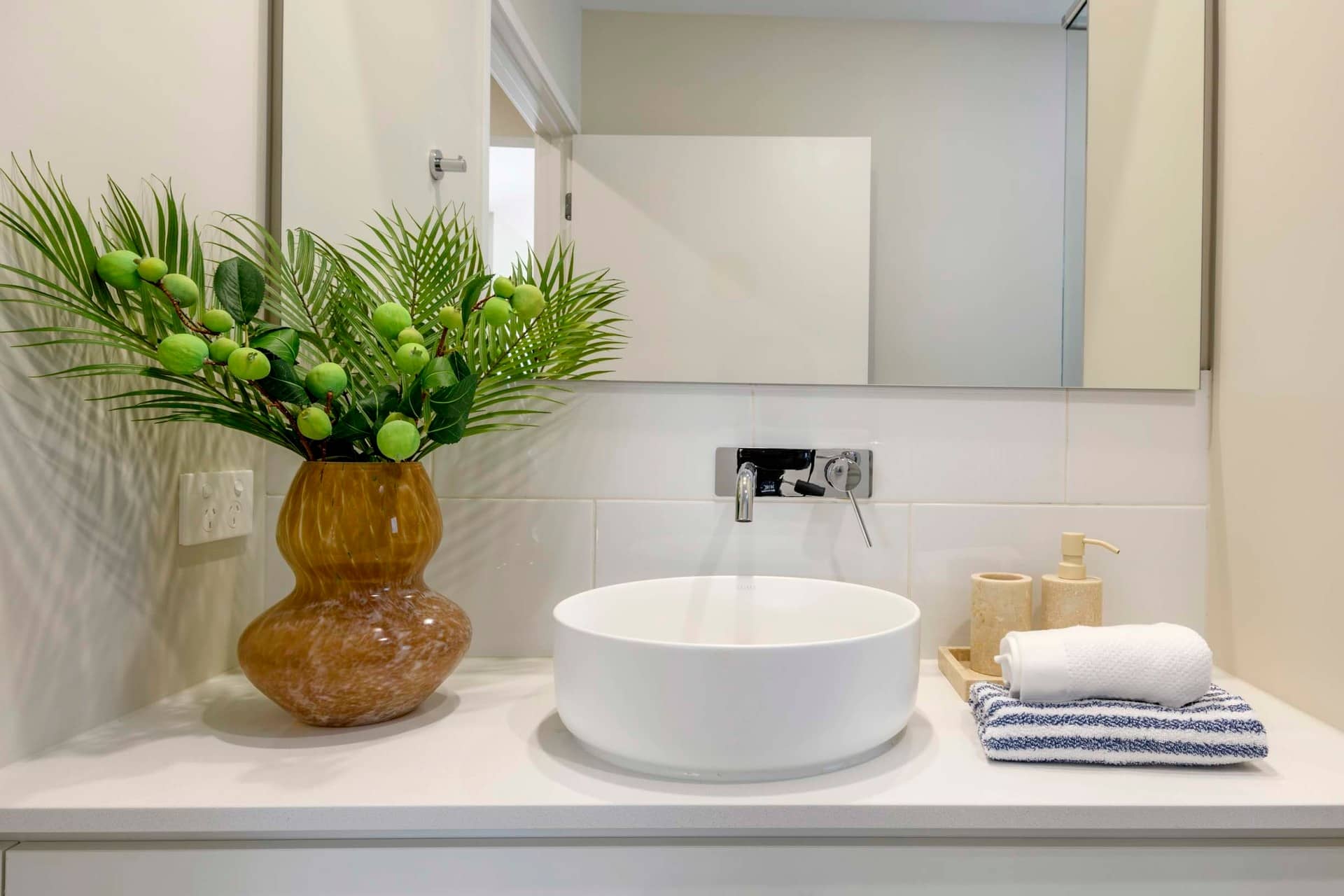 Modern bathroom vanity with a vessel sink, chrome tap, and decorative plant in a brown vase.