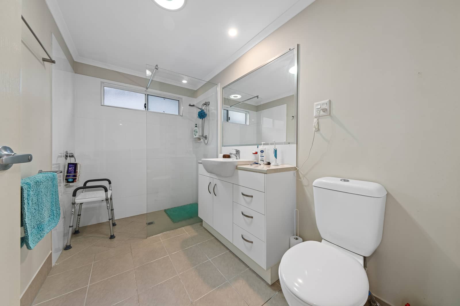 Interior of a bathroom in an Ingenia Lifestyle home, featuring a shower with glass screen, vanity, toilet, and shower chair.