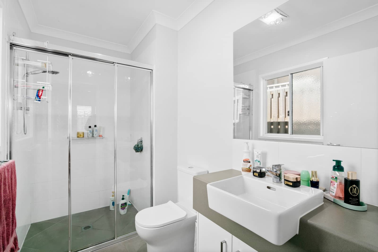 A bright, modern bathroom with a glass-enclosed shower, white toilet, and vanity with a white sink.
