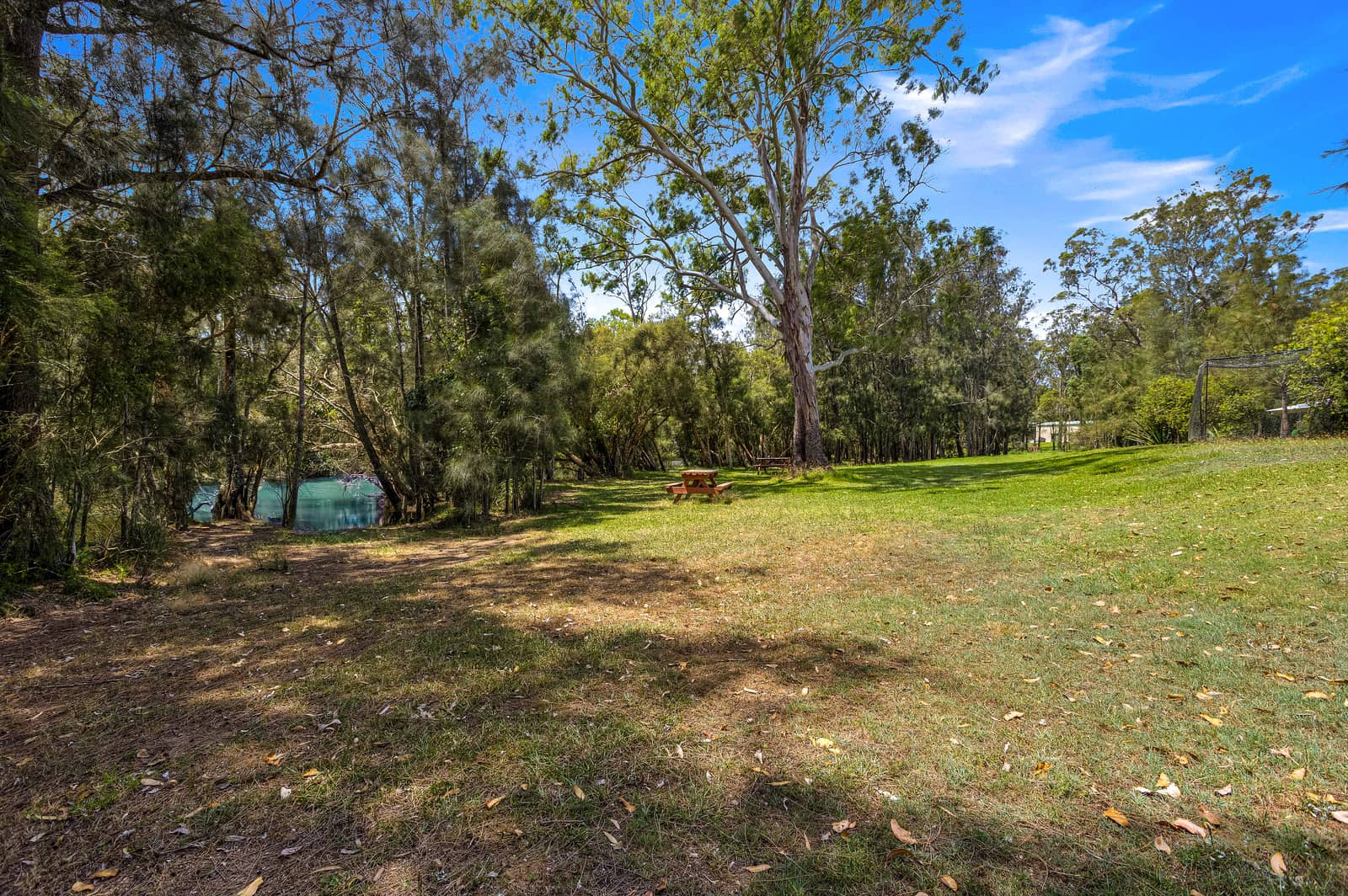 A picnic table is set on a grassy area beside a tranquil body of water, surrounded by lush trees.