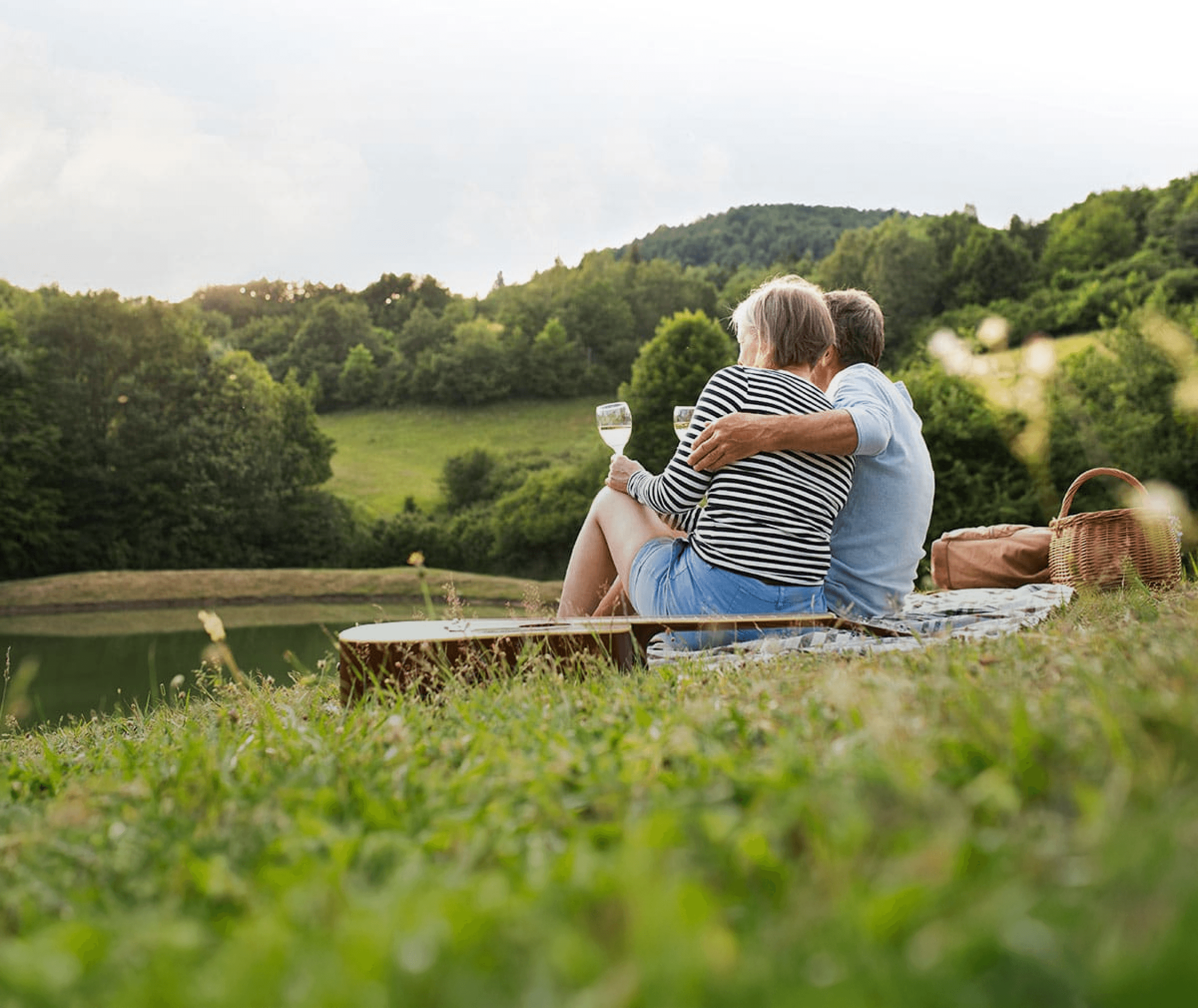 Two people picnicking on grassy grounds by a lake, with a guitar and wine, enjoying the outdoors at an Ingenia Lifestyle community.