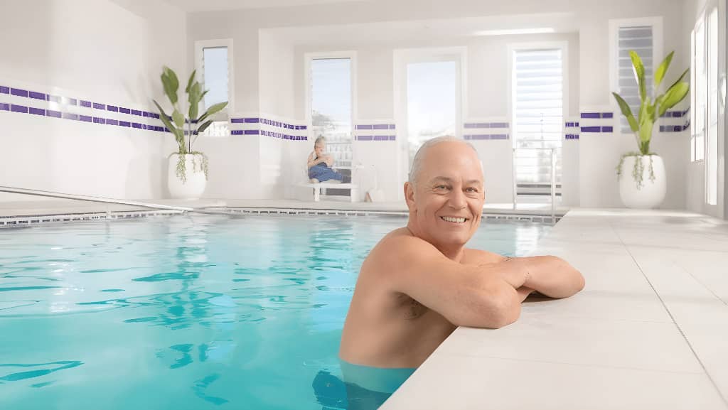 A man smiling in a bright indoor swimming pool, part of an Ingenia Lifestyle community's shared facilities.