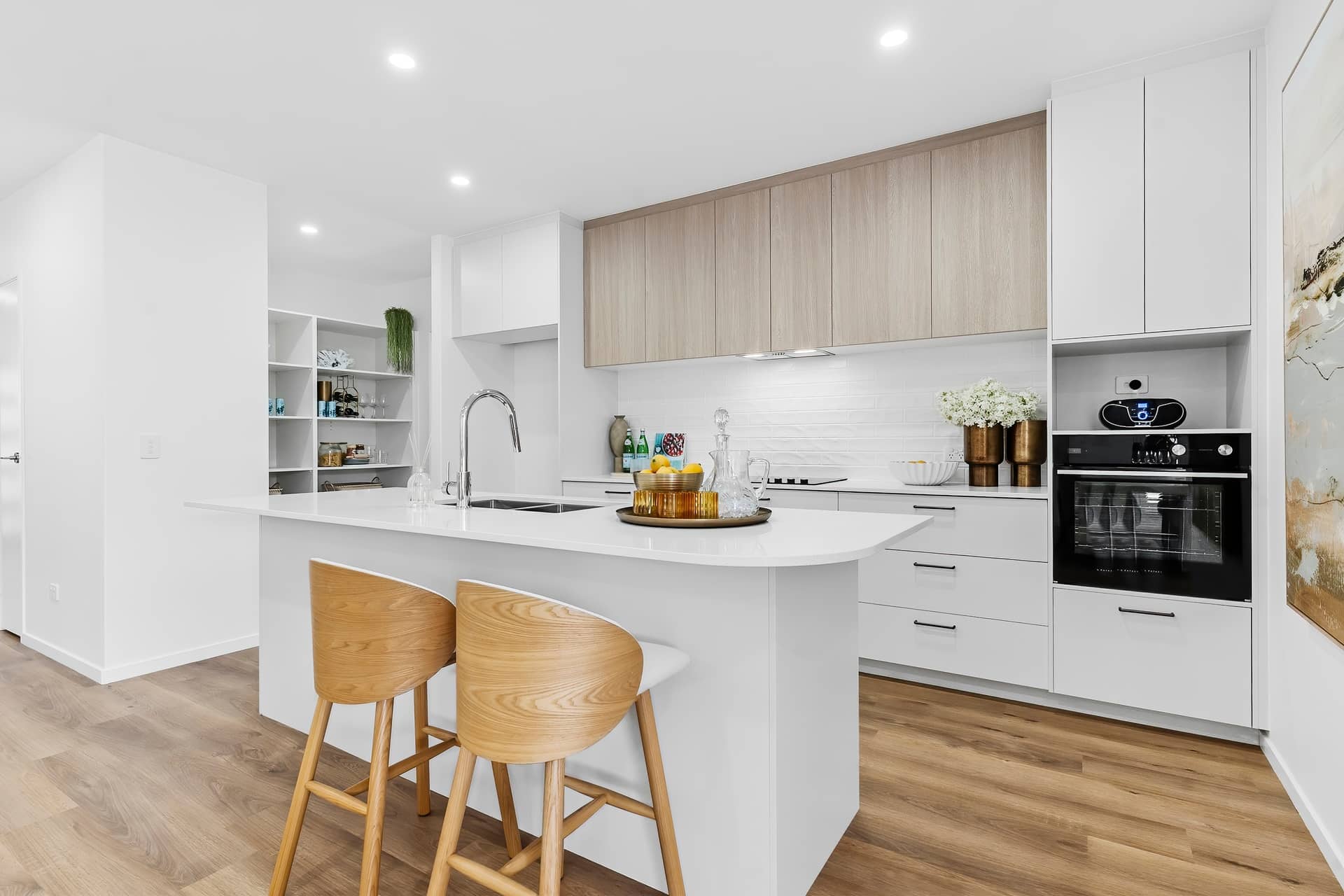 Modern kitchen with island, white countertops, light wood cabinetry, and two wooden bar stools.