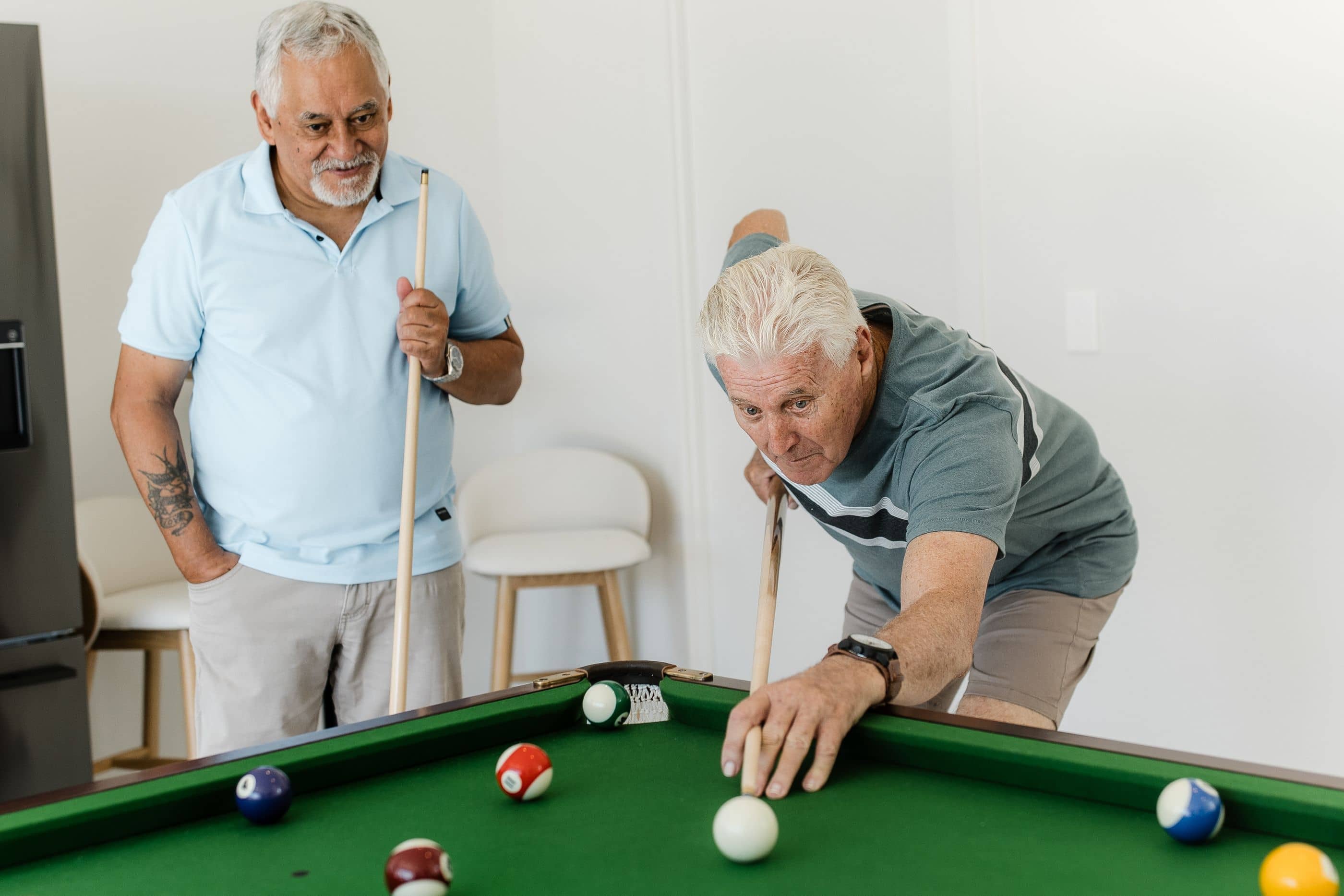 Two individuals playing pool on a green table, one lining up a shot as the other watches in an Ingenia Lifestyle shared facility.