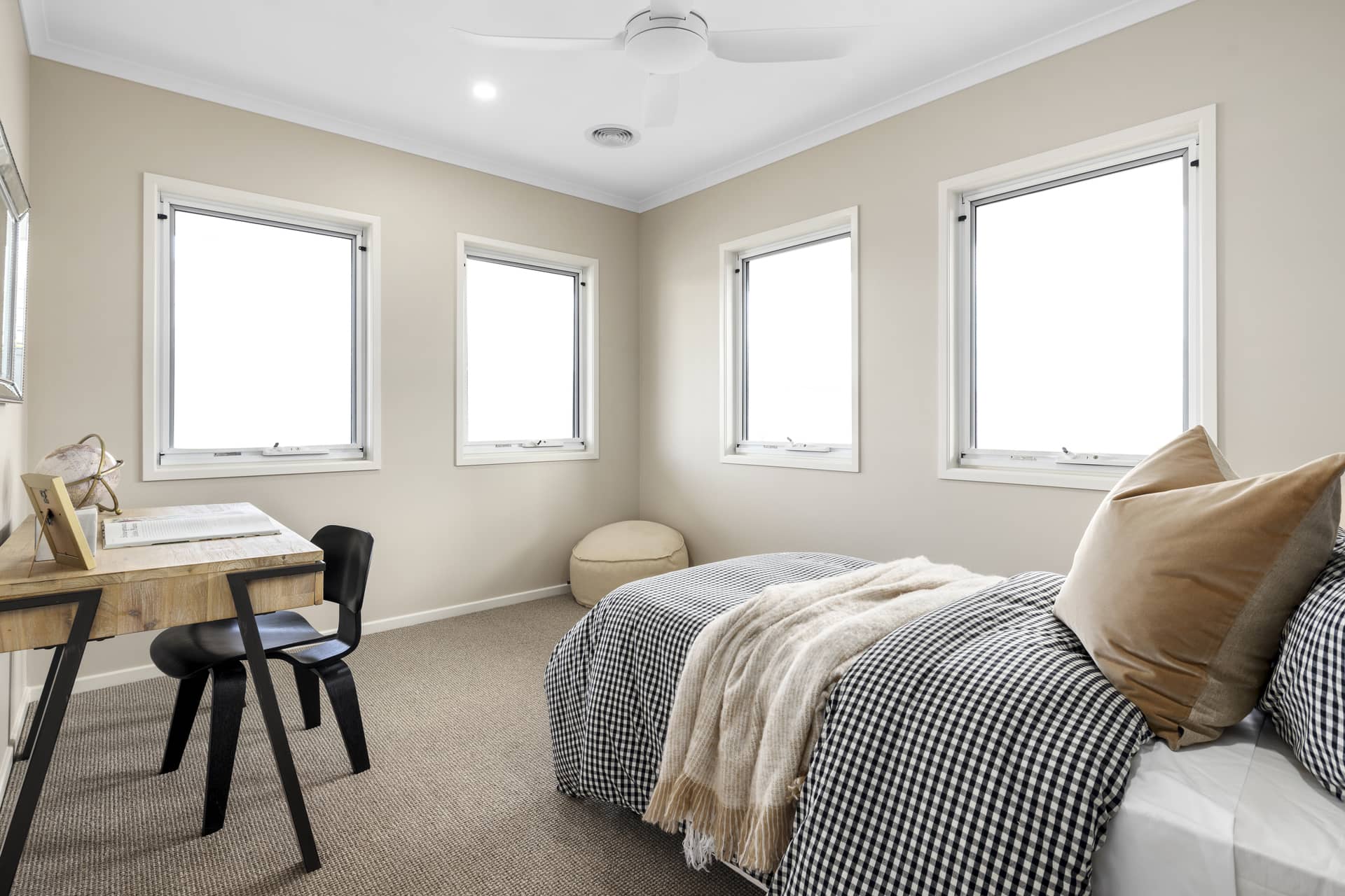 A bedroom with a bed, desk, chair, and ceiling fan in a neutral-toned room.