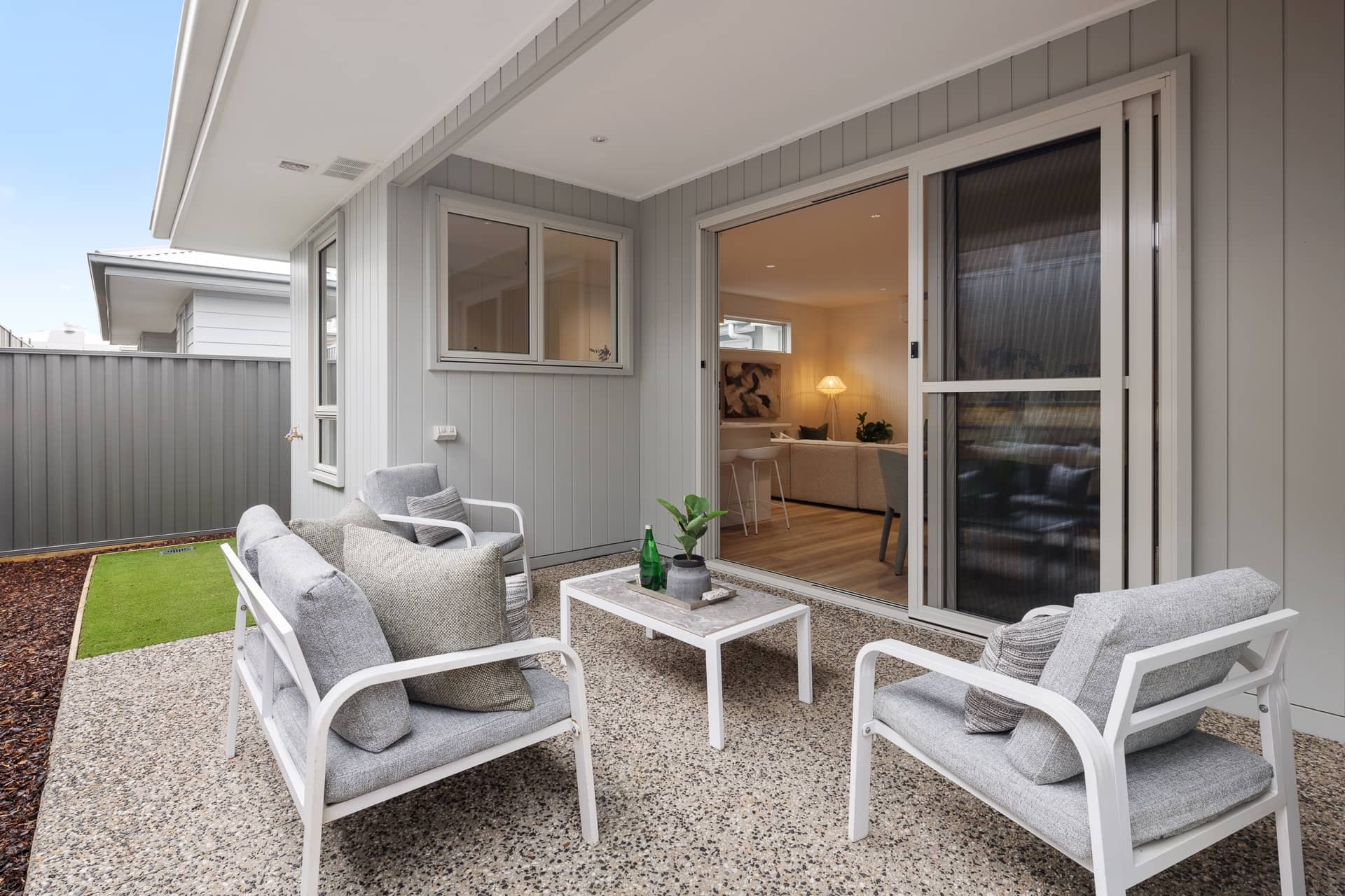 An Ingenia Lifestyle home's outdoor patio with grey seating, a coffee table, and sliding doors to the living room.