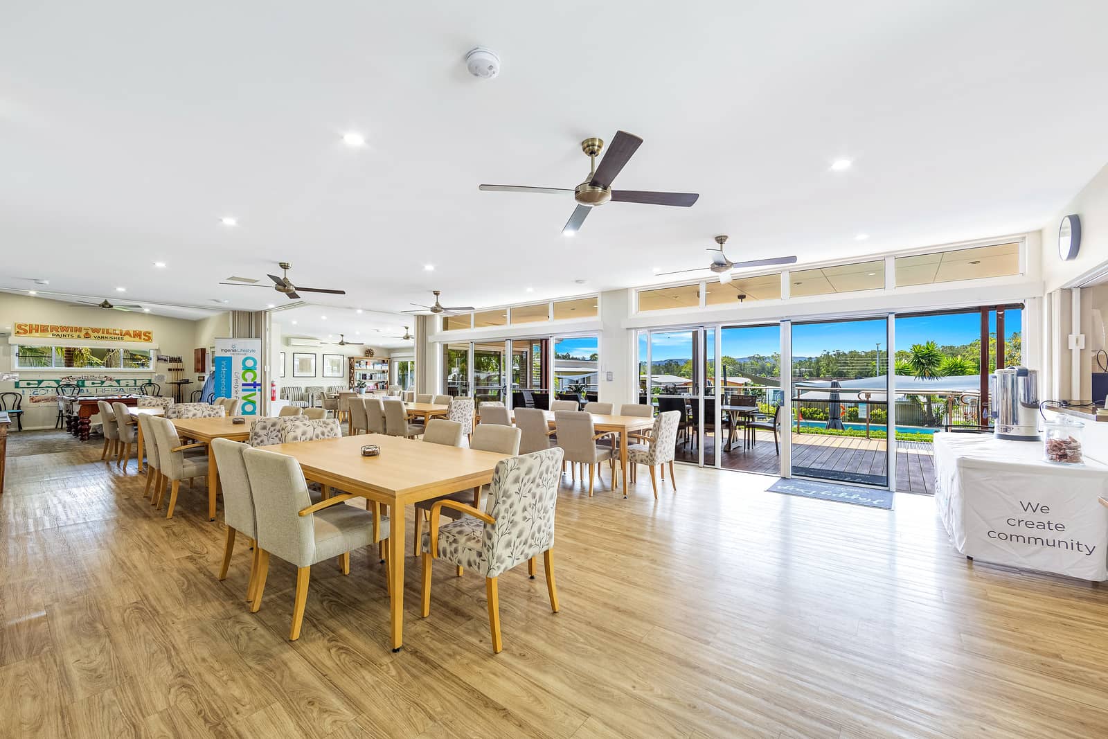 Spacious dining hall with multiple tables and chairs, and large sliding doors opening to a view of a pool and landscaped grounds.