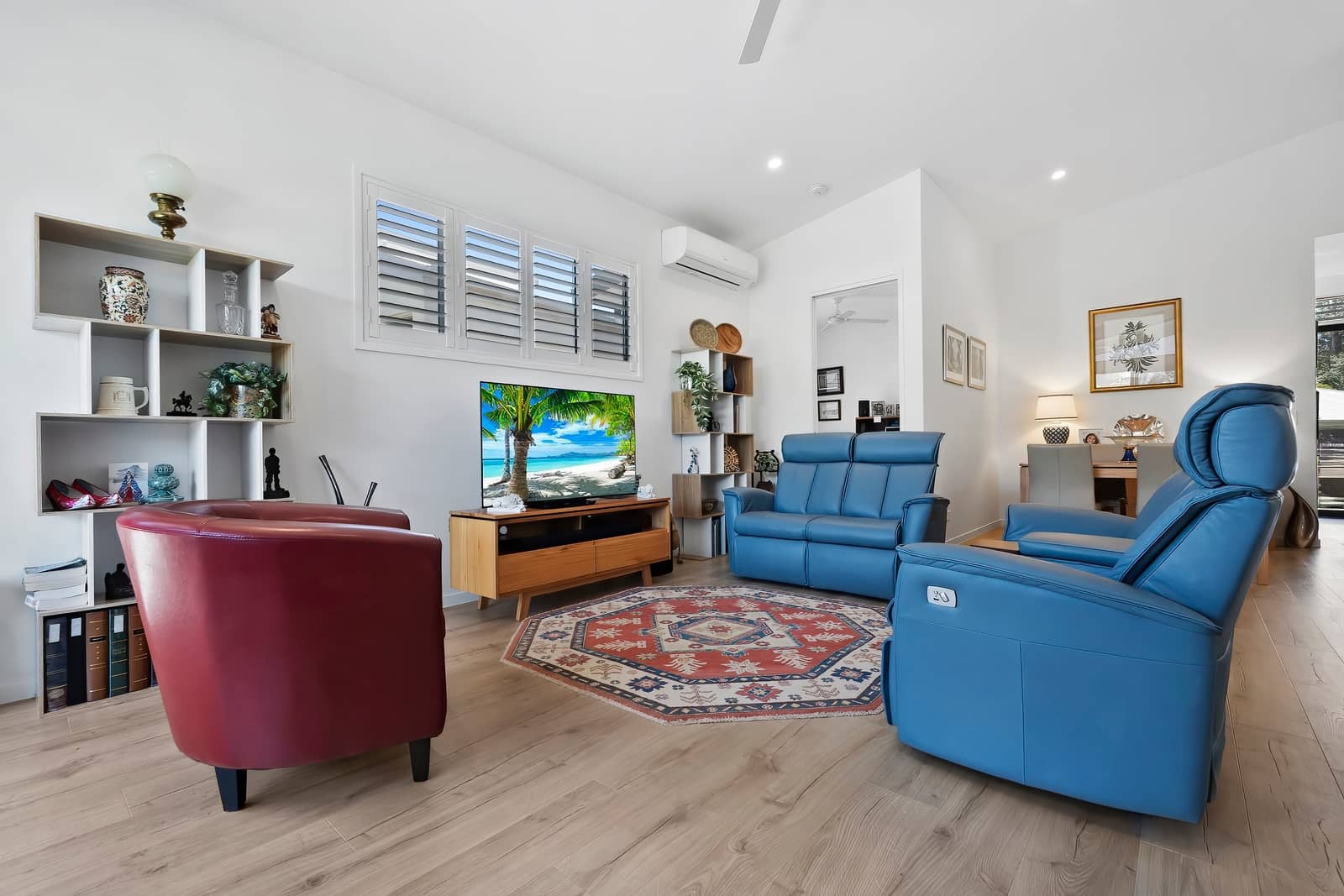 Bright living room of an Ingenia Lifestyle home, featuring a blue recliner and sofa, red armchair, TV, and dining area beyond.