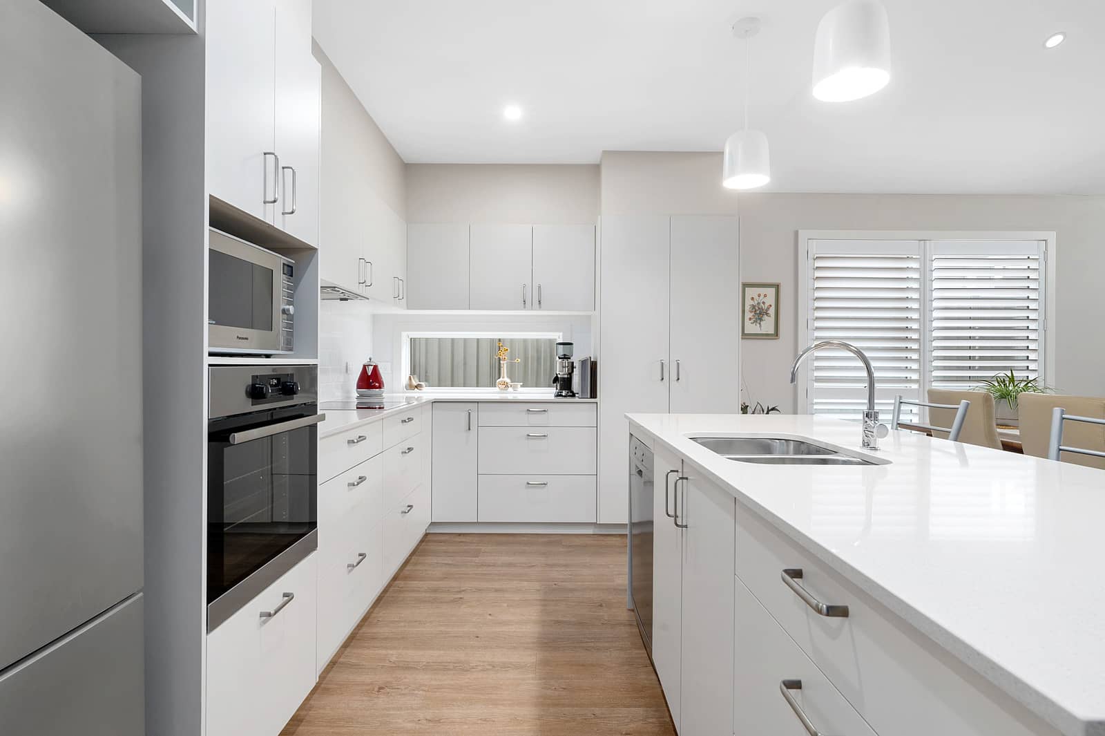 Modern white kitchen with island, stainless steel appliances, wood-look floor, and clean cabinetry in an Ingenia Lifestyle home.