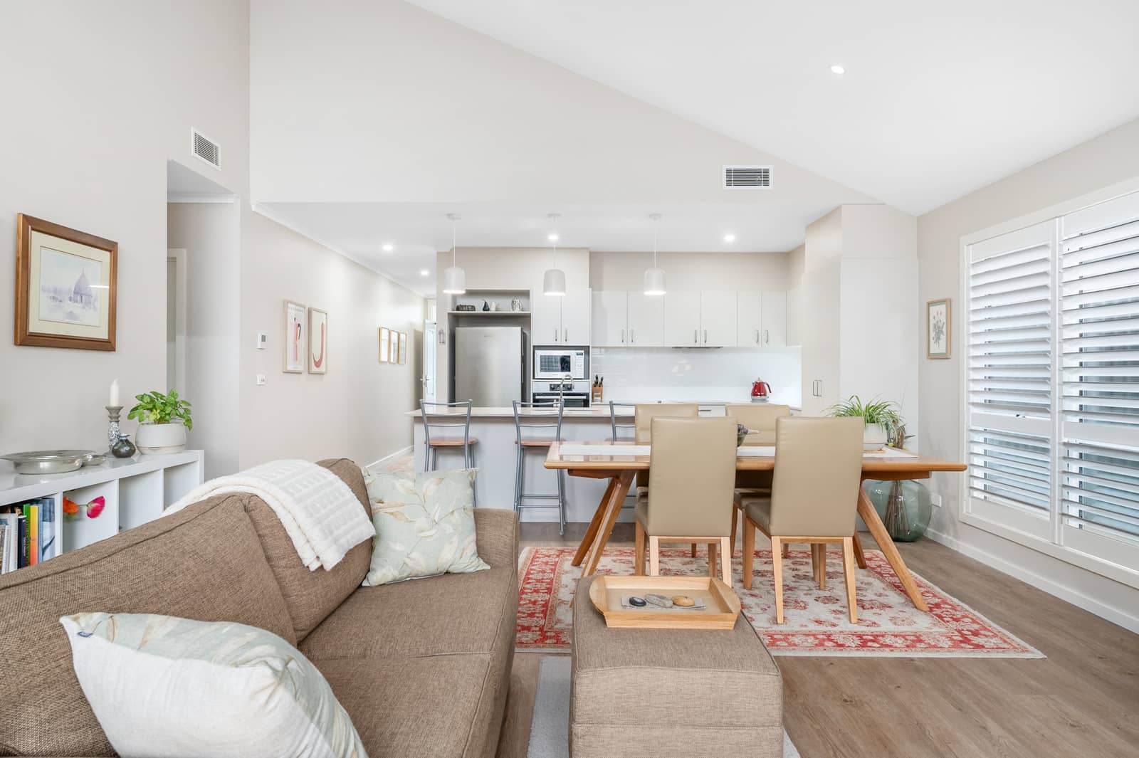 Open-plan living, dining, and kitchen in an Ingenia Lifestyle home with vaulted ceilings, wood floors, and white kitchen.