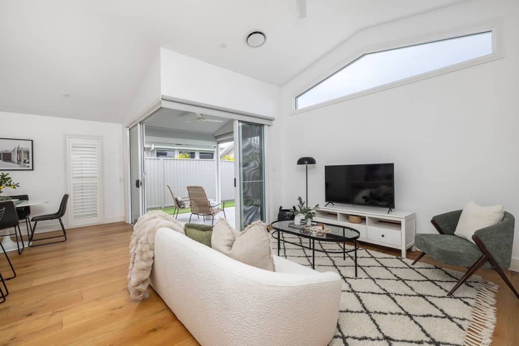 Bright living room in an Ingenia Lifestyle home, with a white sofa, TV, and wooden floors, opening to a private patio.