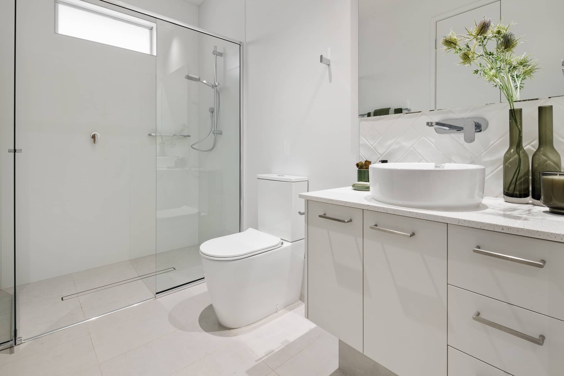 A modern white bathroom in an Ingenia Lifestyle home, featuring a glass shower, toilet, and vanity with round basin and mirror.
