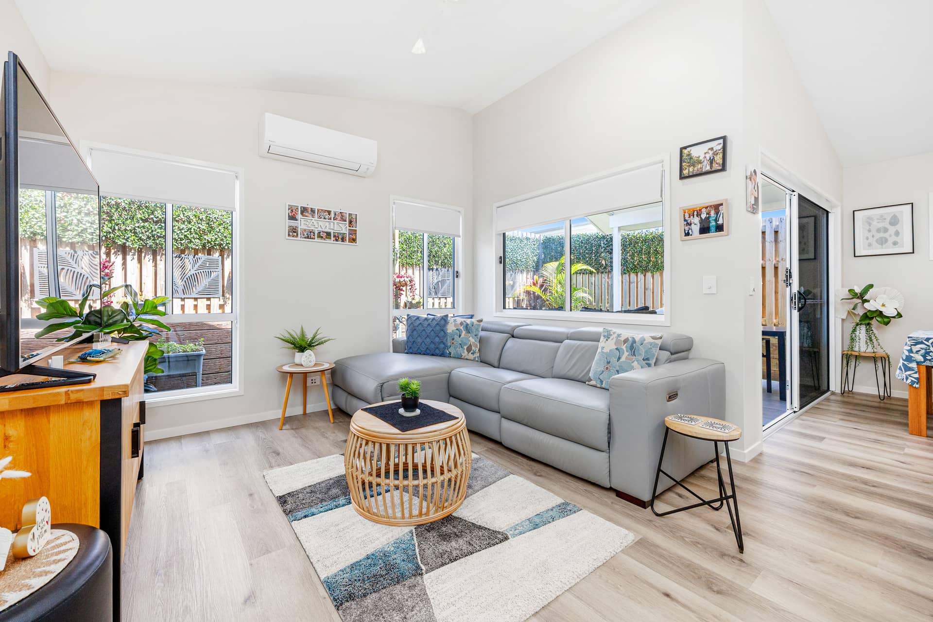 A bright, modern living room in an Ingenia Lifestyle home, featuring a grey sofa, wood-look floor, and windows overlooking a private garden.