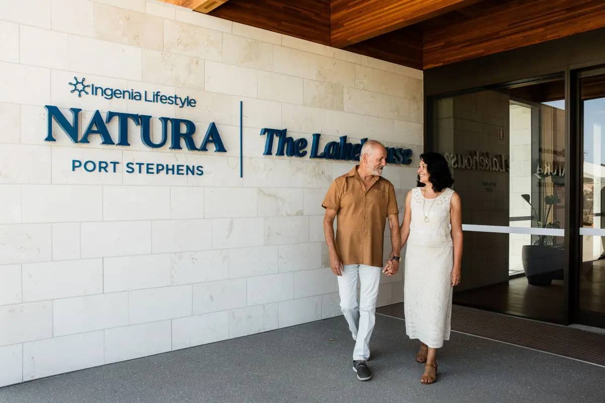 Two people walk past the Ingenia Lifestyle Natura Port Stephens 'The Lakehouse' sign.