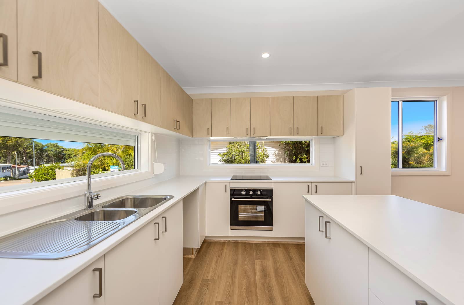 Bright kitchen in an Ingenia Lifestyle land lease home, with light wood cabinets, white countertops, modern appliances, and views of outdoor landscaping.
