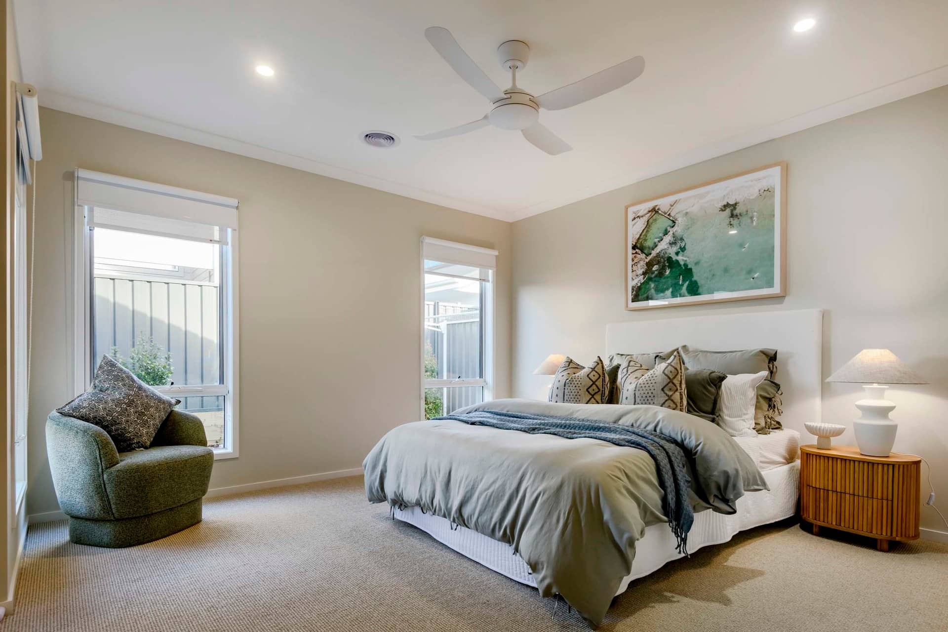 A well-lit bedroom with a large bed, a green armchair, and a framed artwork above the bed.