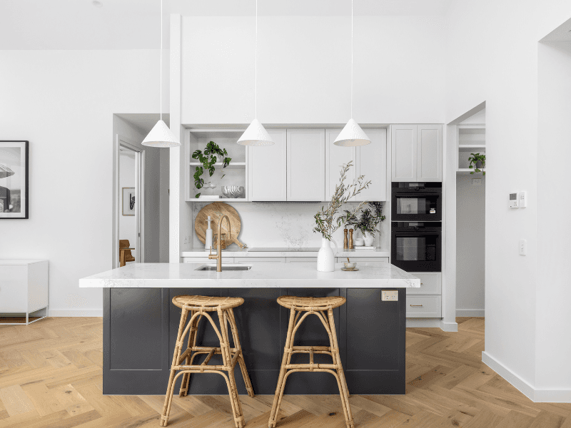 Modern kitchen in an Ingenia Lifestyle home with a dark island, white countertops, integrated ovens, and timber flooring.
