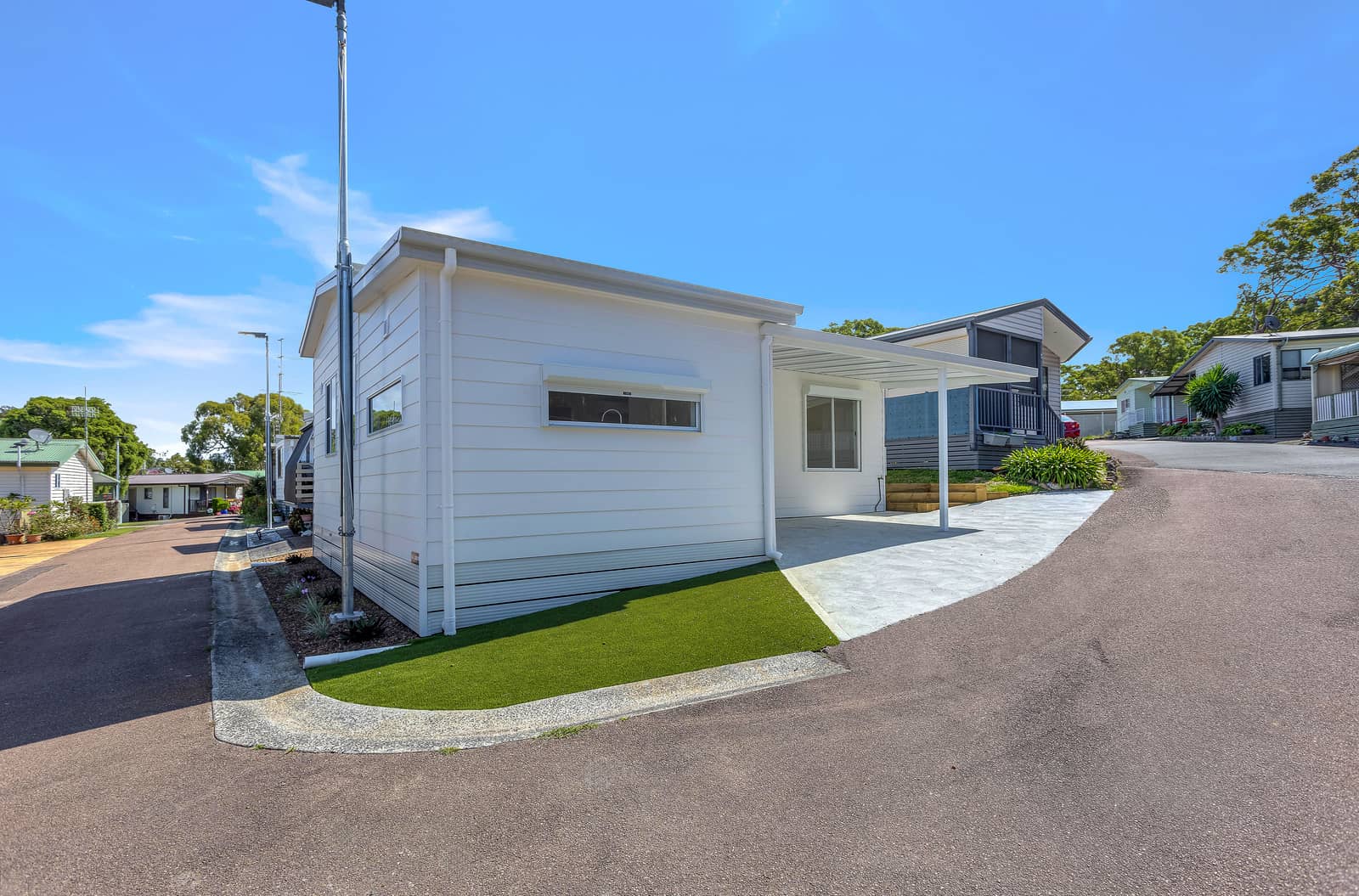 A white land lease home with a carport, artificial turf, and a concrete path in an Ingenia Lifestyle community.