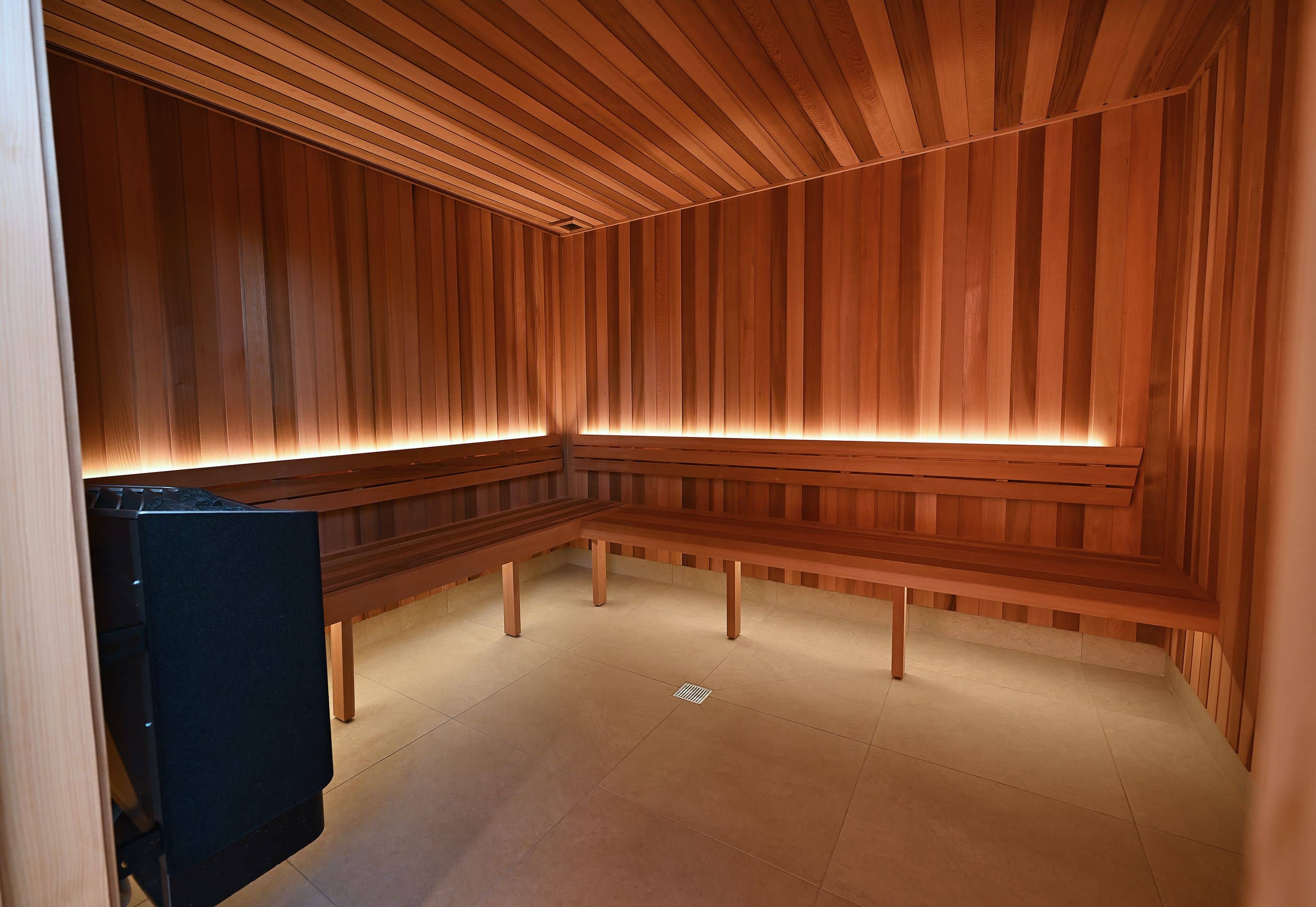 Interior of a modern sauna with wood paneling, benches and a sauna heater.