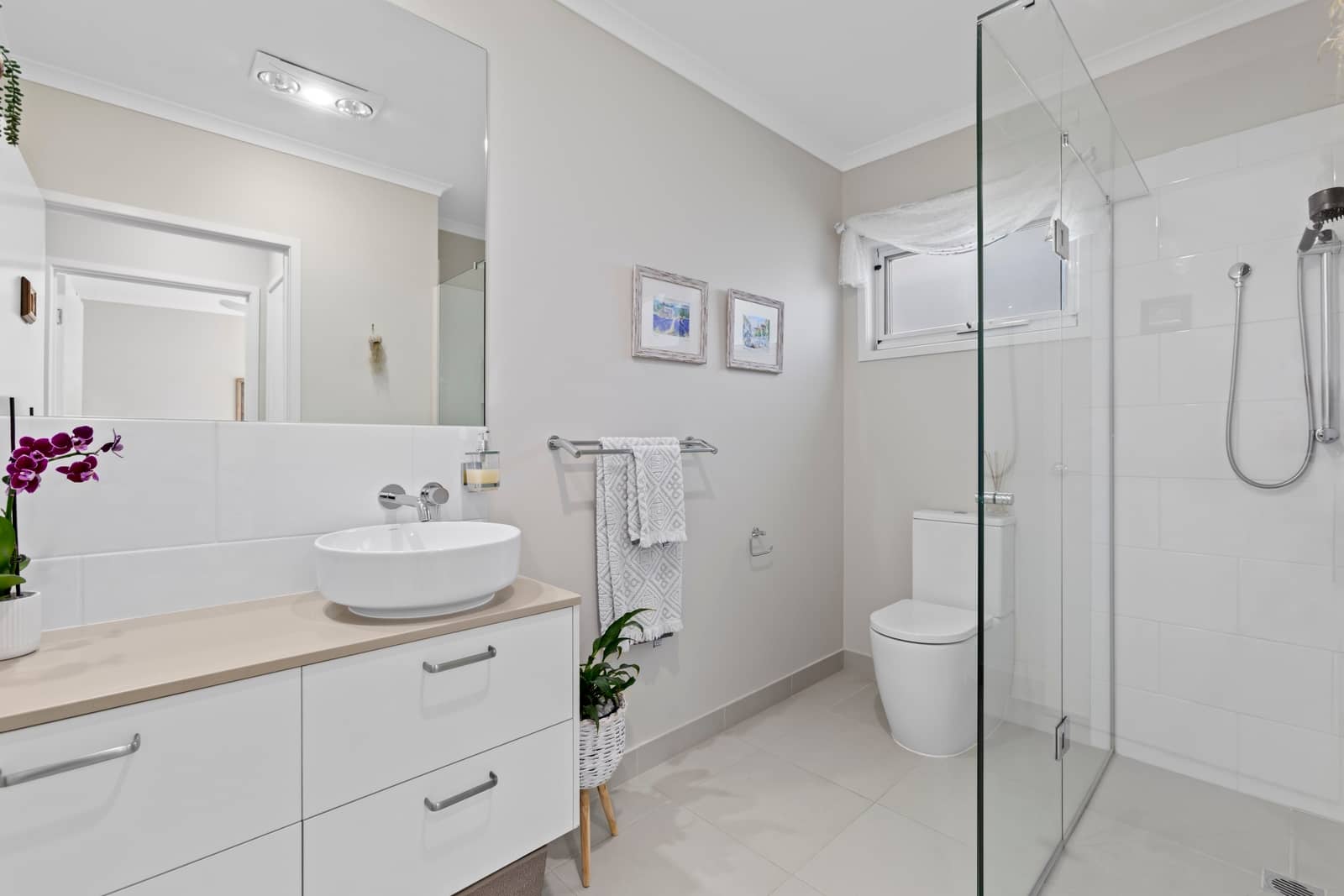 A modern bathroom with a white vanity, basin, toilet, and a glass-enclosed shower.