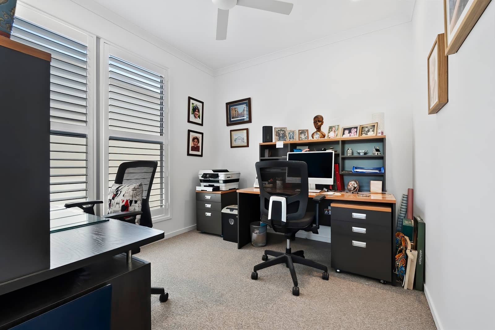 A bright home office in an Ingenia Lifestyle home, with two desks, chairs, a computer, printer, and white plantation shutters.