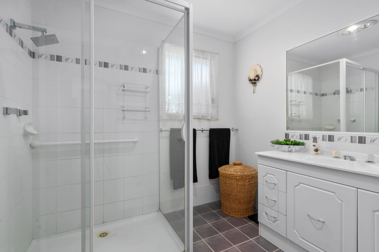 A white-tiled bathroom in an Ingenia Lifestyle home featuring a glass shower with grab rails and a white vanity with storage.